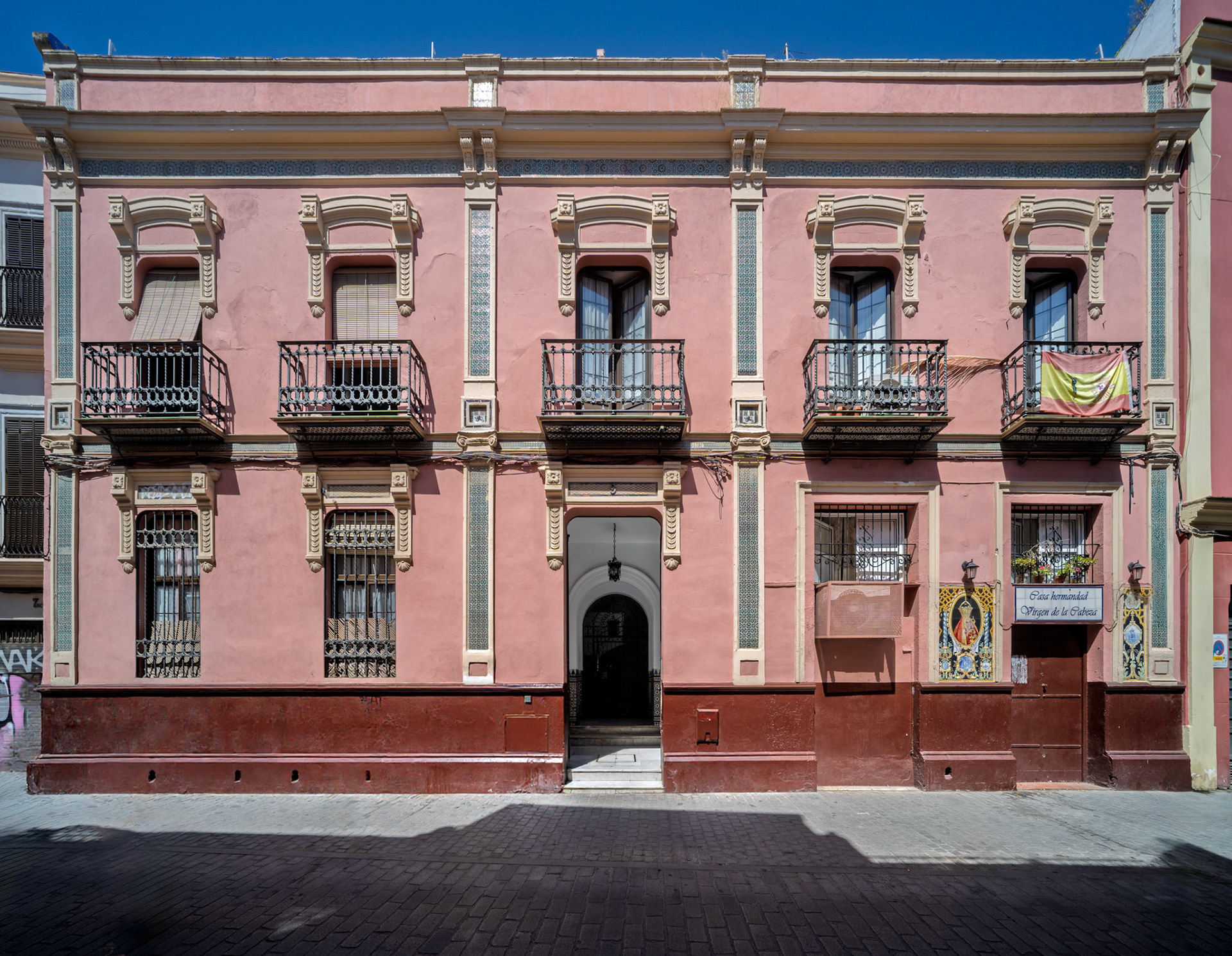 This modernist house on San Luis Street boasts a symmetrical facade, floral stucco, and ornate wrought iron balconies amid Seville's history.