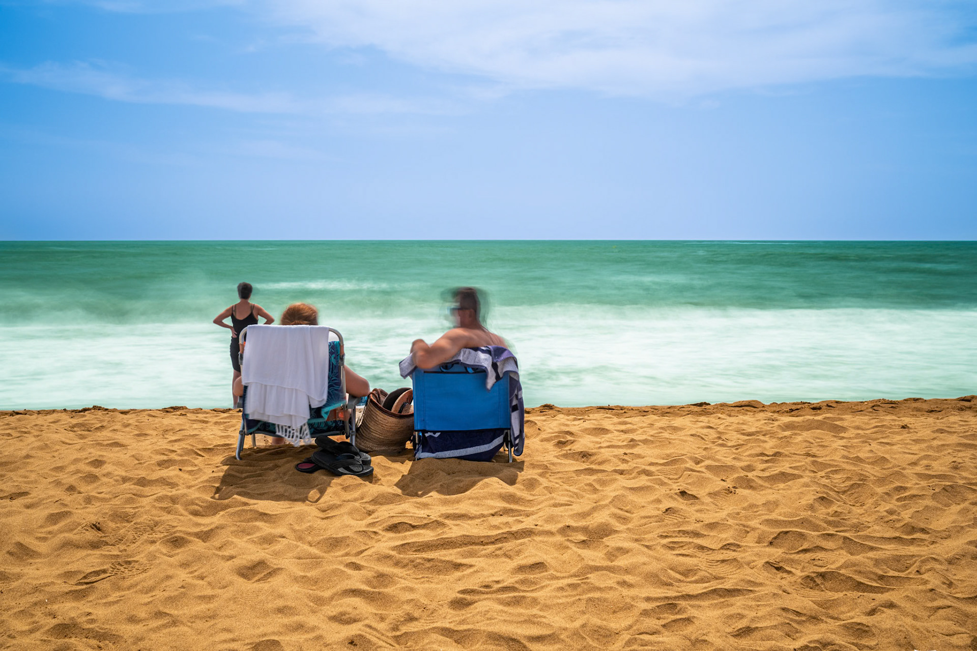 Visitors enjoy a sunny day at Isla Canela beach in Ayamonte, capturing the calm waves with stunning long exposure photography.