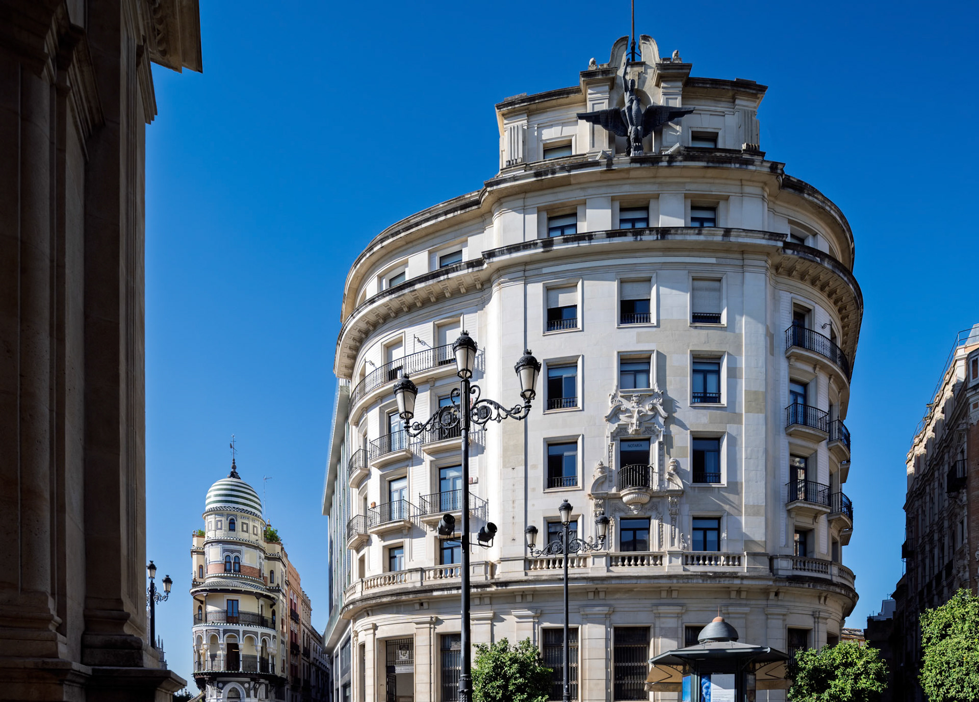 The Unión y el Fénix and Adriática buildings seen from Plaza Nueva—curved stone facades, sculpted balconies, and rooftop statuary rise above the avenue,