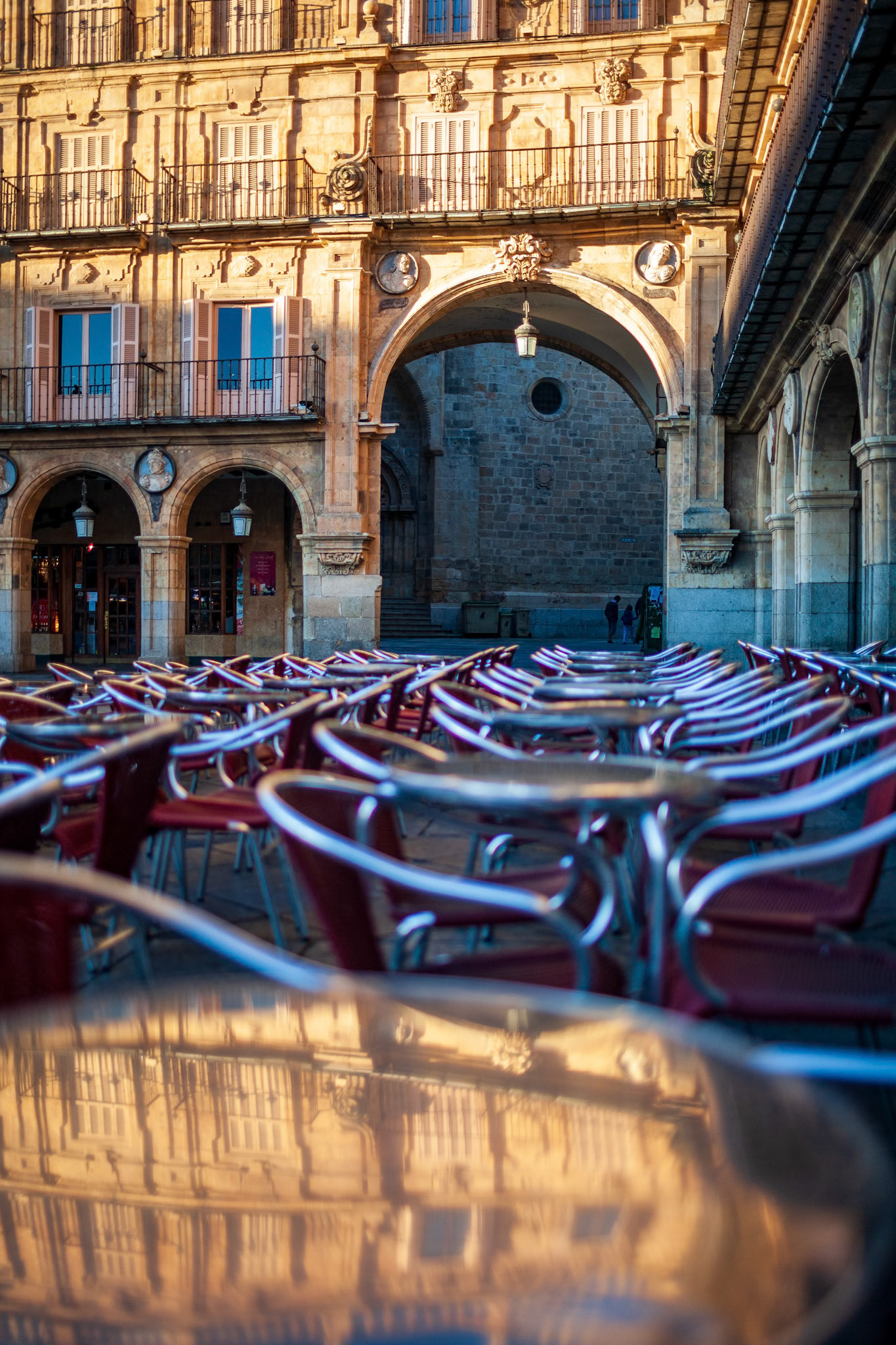 Cafe tables in Plaza Mayor of Salamanca reflecting morning light and architectural details.