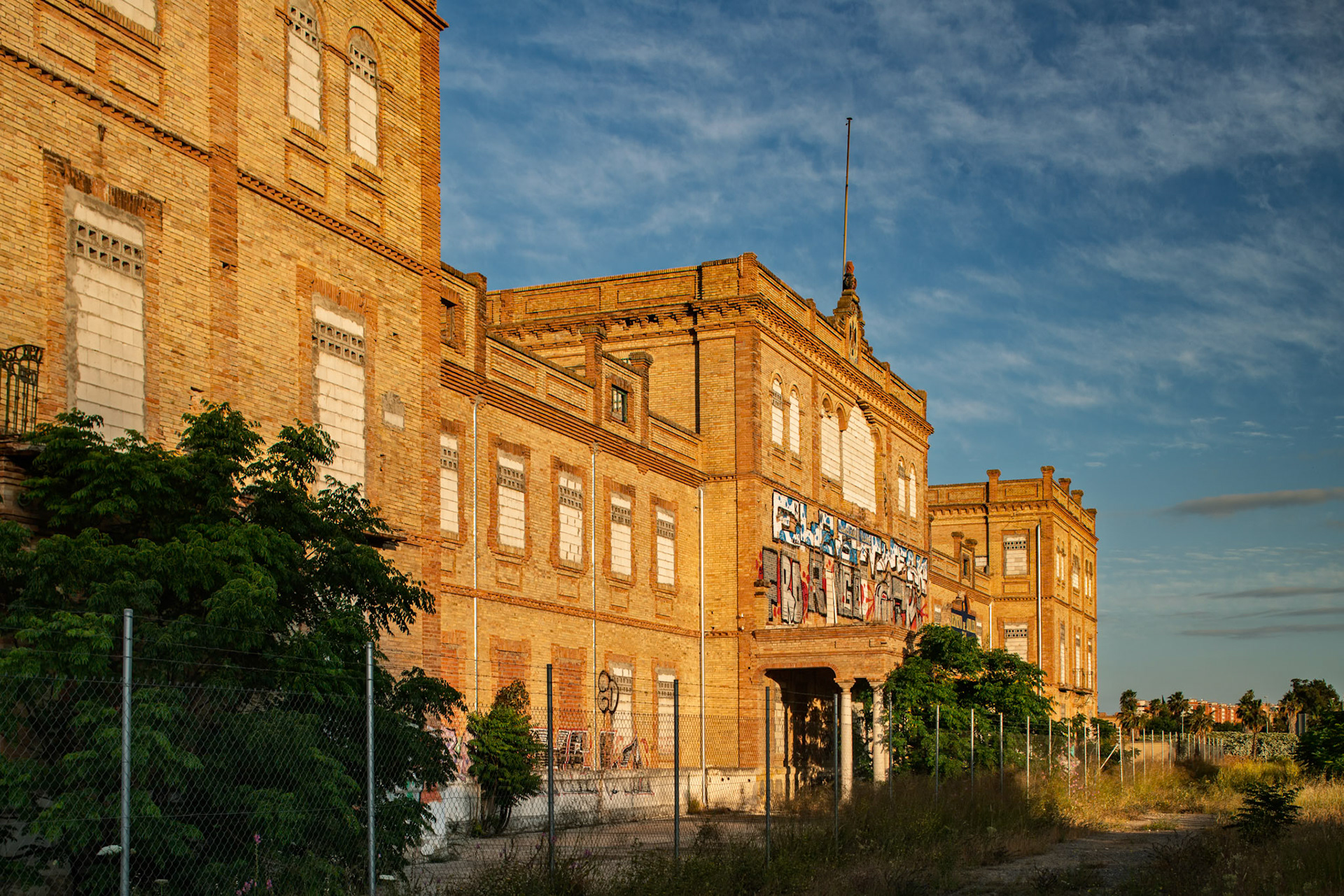 The abandoned RACA 14 Artillery Regiment in Seville displays its historic architecture and intriguing graffiti beneath a blue sky.