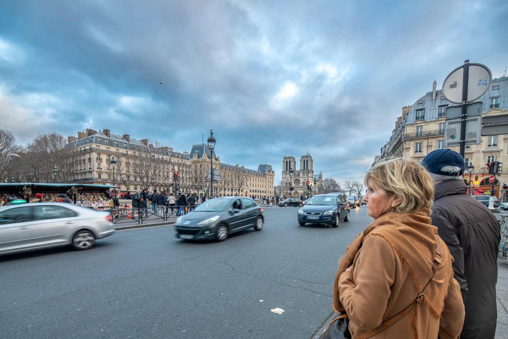 A couple standing in the street with Notre Dame in the background on Quai Saint Michel Street in Paris, France.