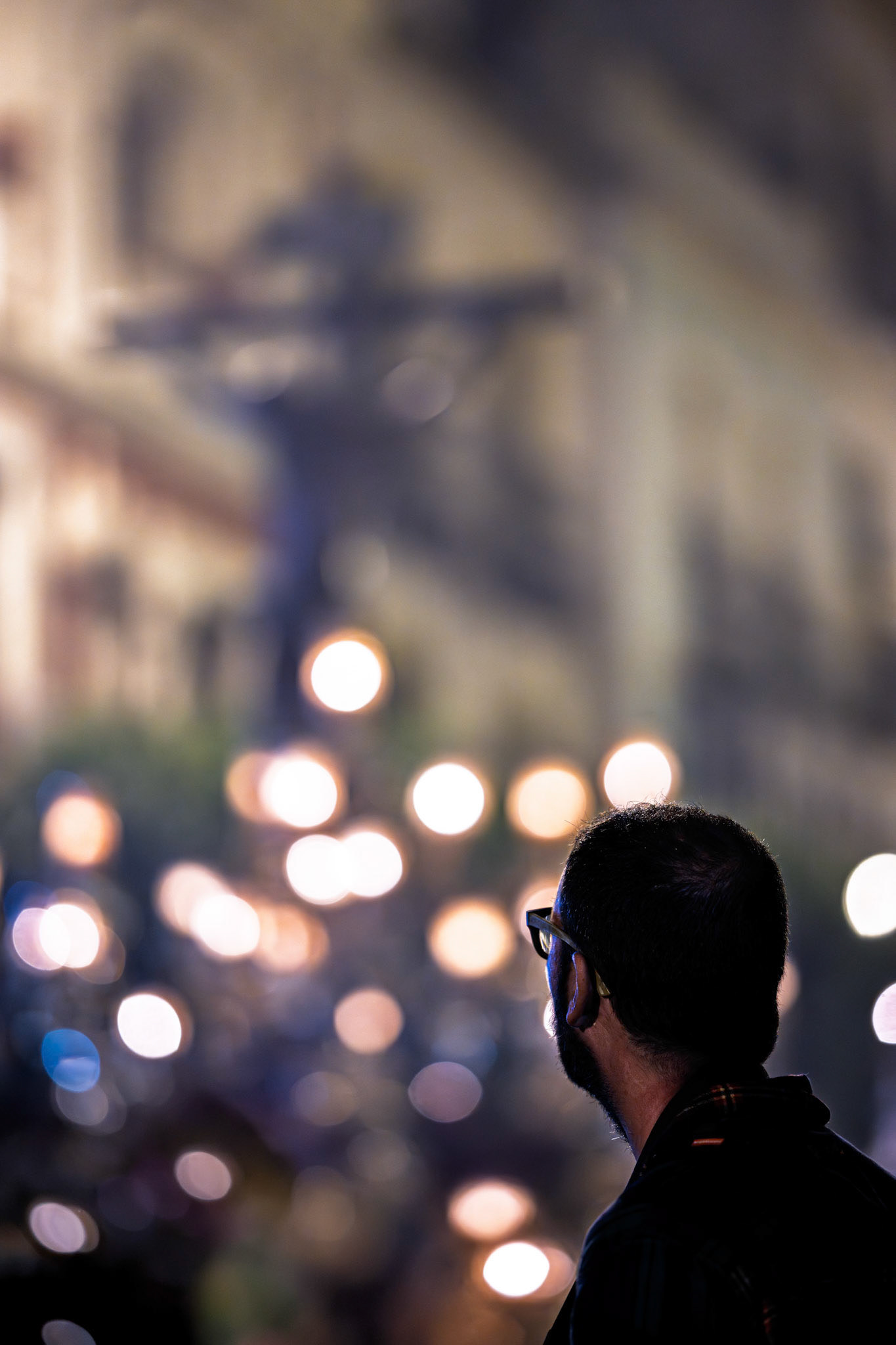 A man watches a crucified Christ statue on a float during a Holy Week procession at night in Seville, Andalusia, Spain. Selective focus, bokeh background.