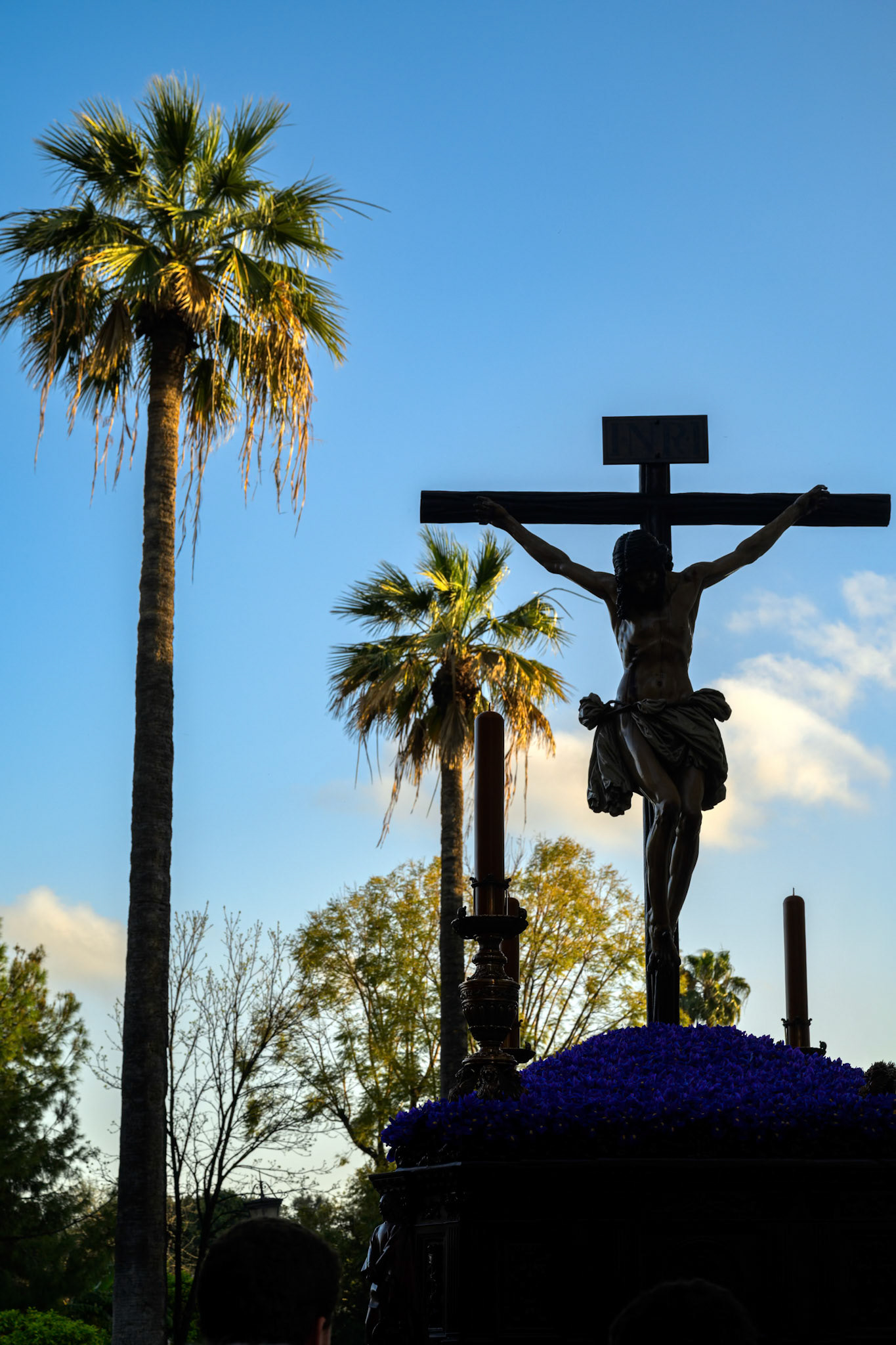 Palm trees stand against the evening sky as the Christ of Buena Muerte (Good Death) processes through Seville during Holy Week.