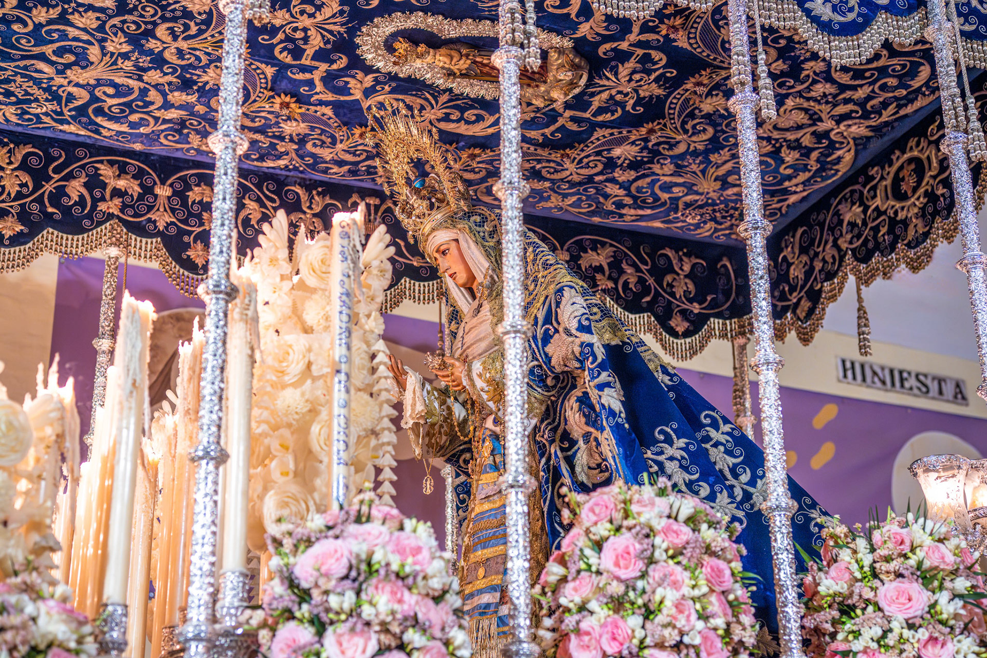 The canopied float of the Virgin of Hiniesta processes along Hiniesta Street during Holy Week in Seville, Andalusia, Spain. Decorated with candles and flowers.