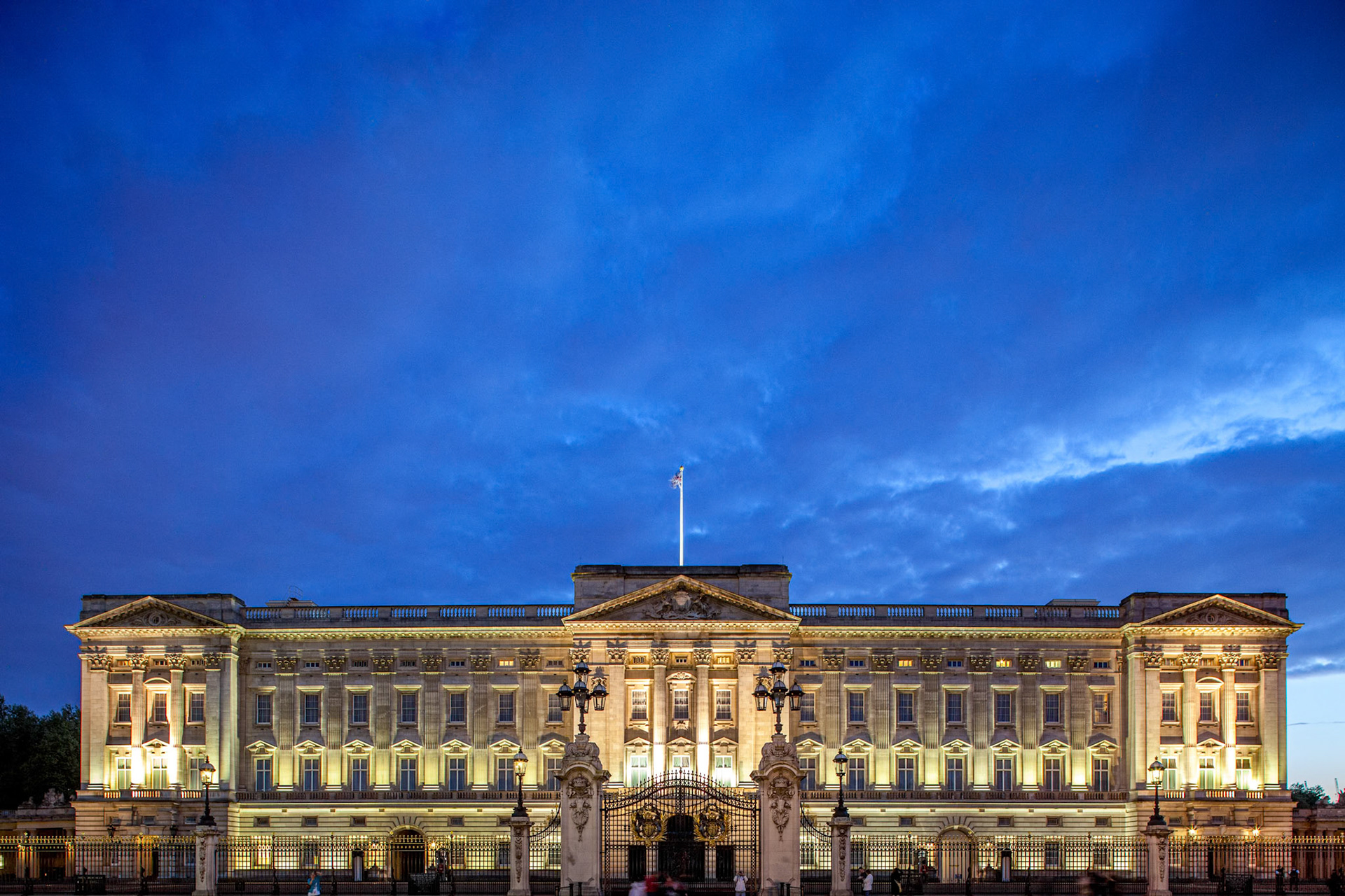 Buckingham Palace illuminated at dusk under a soft blue sky.