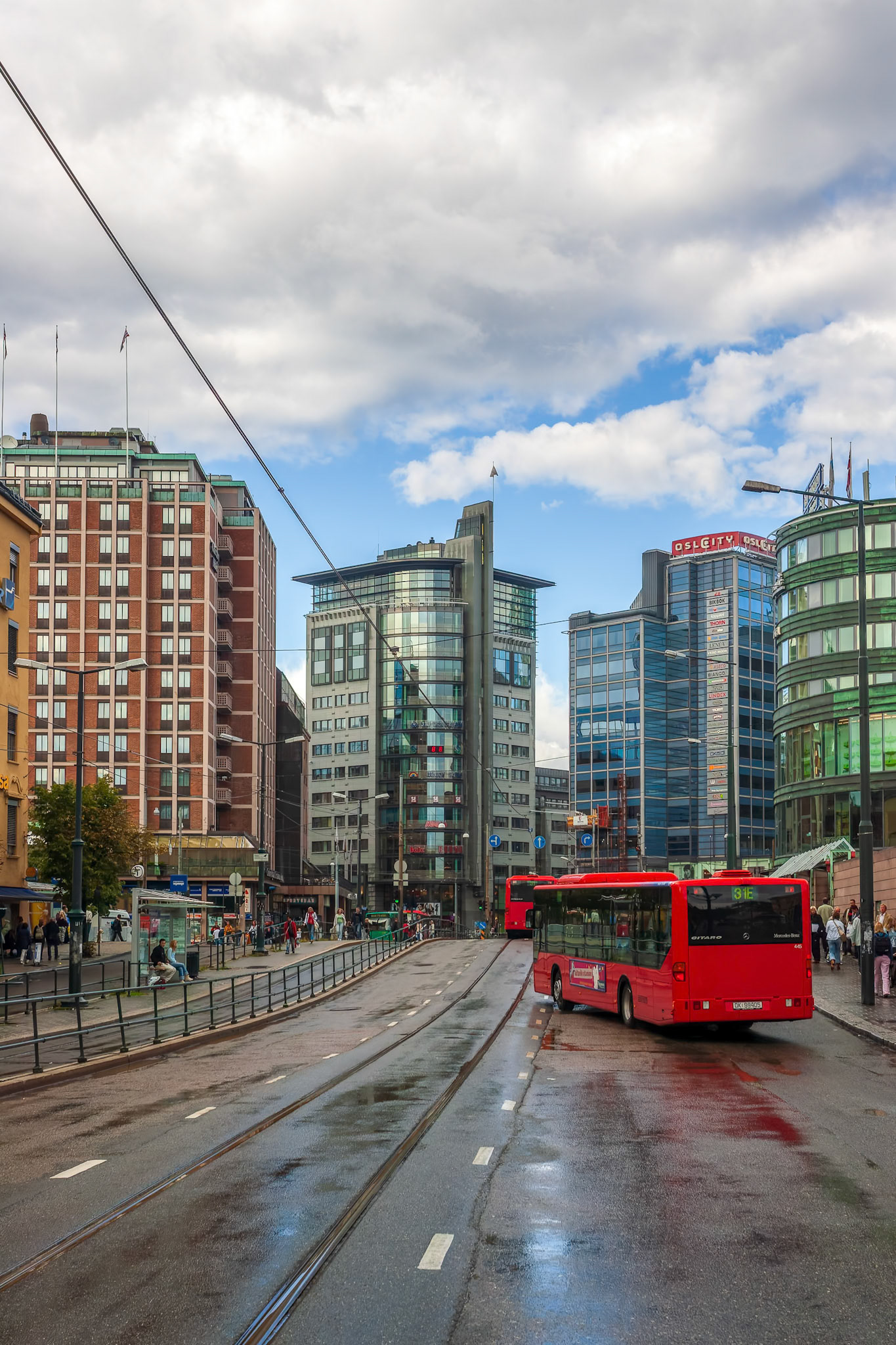 Contemporary buildings line Biskop Gunnerus street in Oslo, showcasing urban life on a cloudy day with people and transportation present.