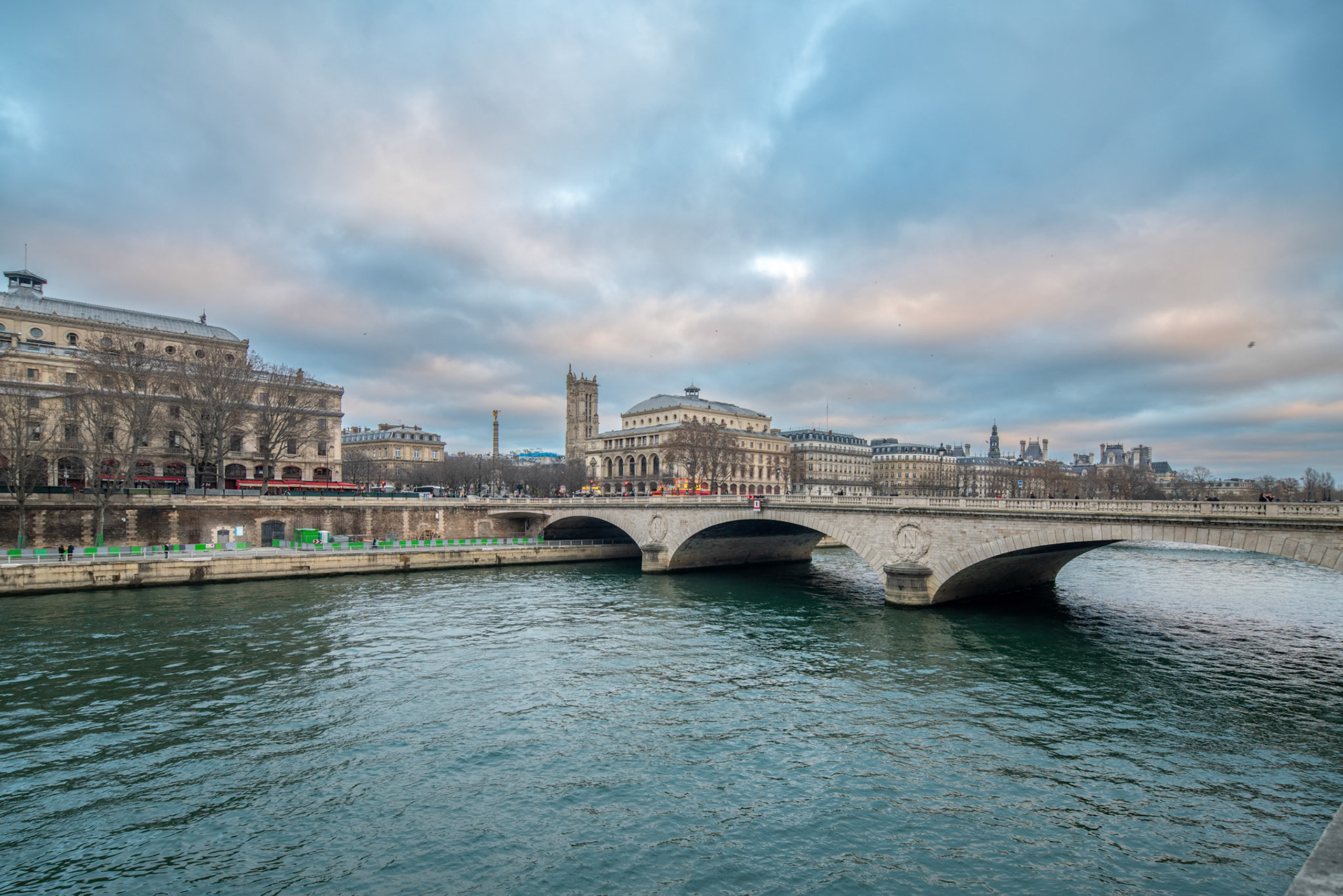 Au Change bridge crossing a body of water with buildings in the background, including the Saint Jacques Tower, in Paris, France.
