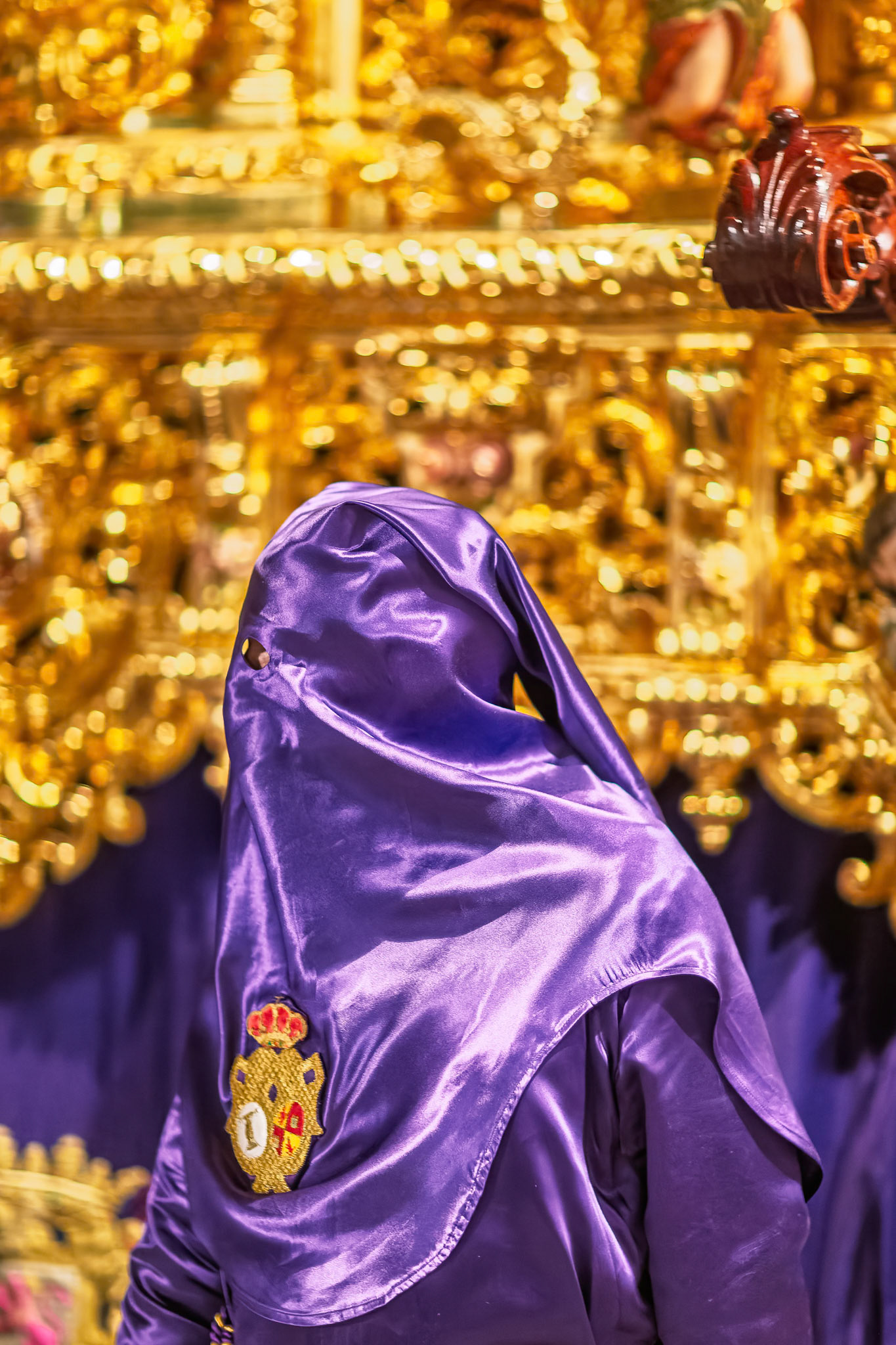 A penitent in a purple robe stands beside the intricately decorated paso de misterio float during Holy Week in Seville, Andalusia.