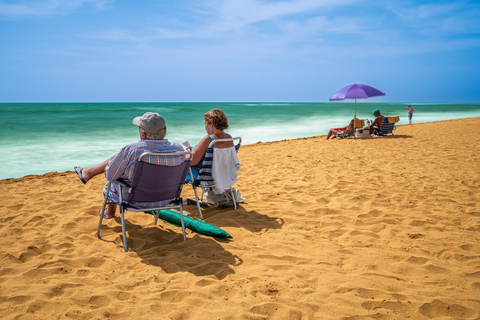 Visitors enjoy a sunny day at Isla Canela beach in Ayamonte, watching the long exposure waves gently wash over the golden sand shoreline.