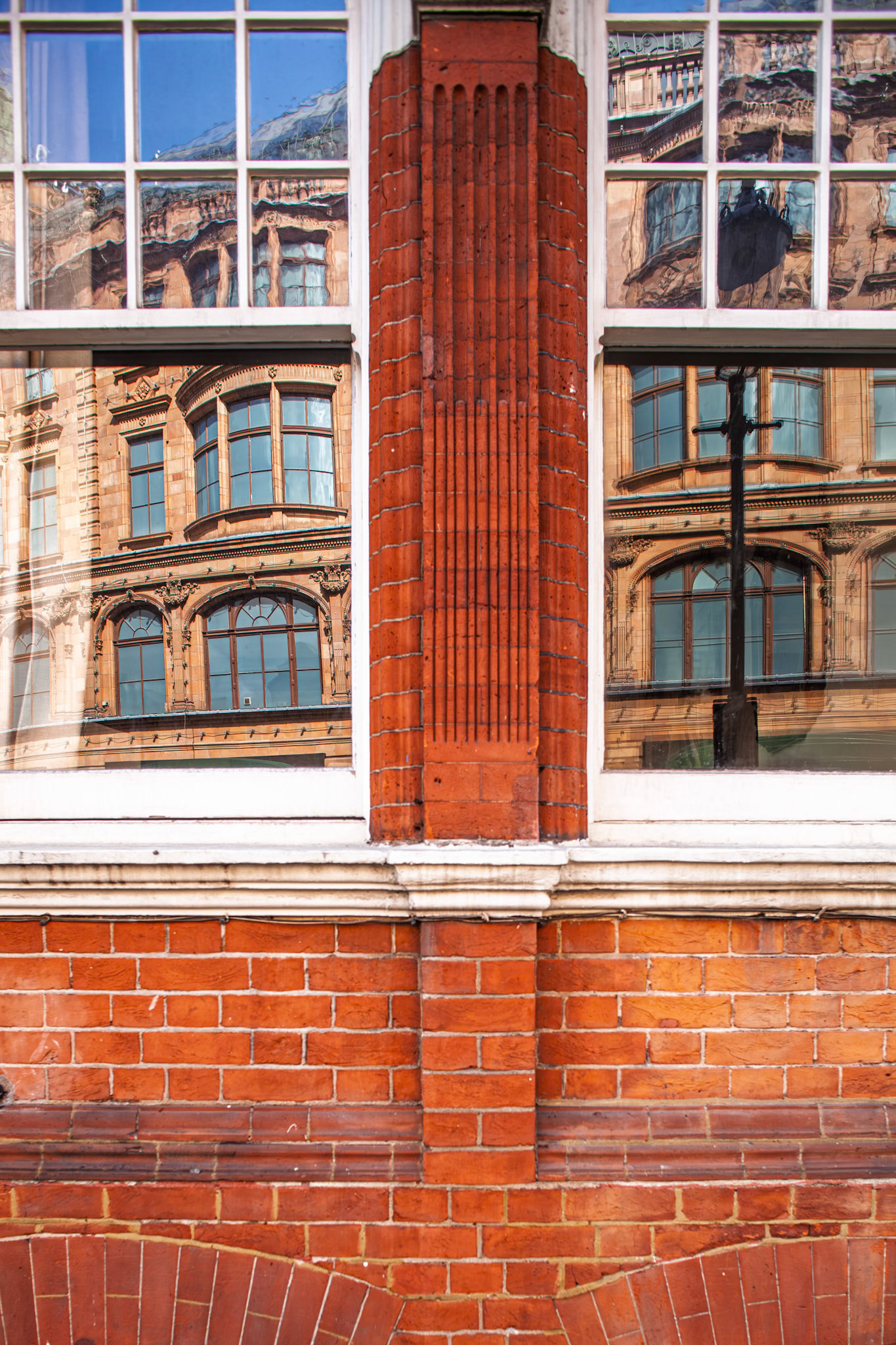 Reflections of the Harrods building appear on the opposite window of another building on Hans Road in London, showing bricks and glass.