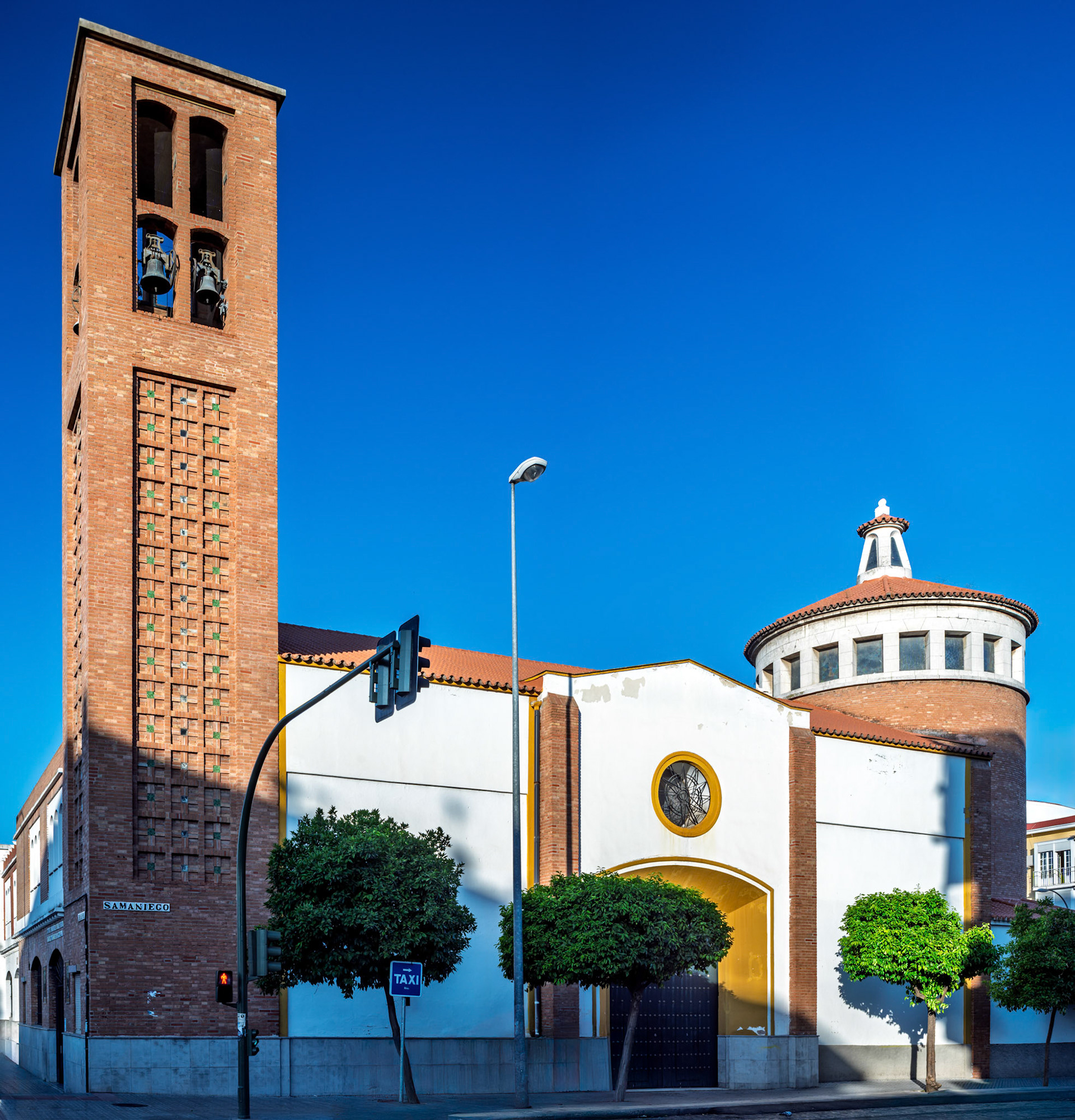 The Church of San Jose Obrero in Seville boasts a tall bell tower and a striking triple nave, showcasing mid-20th-century Spanish architecture.