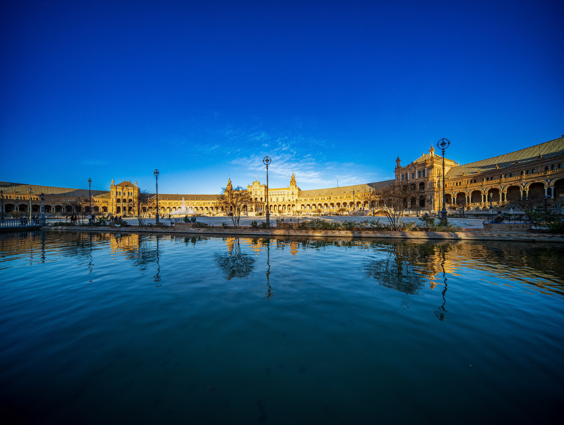 The central section of Plaza de Espana showcases a stunning wide angle view under clear winter light, with arches mirrored in the tranquil canal.