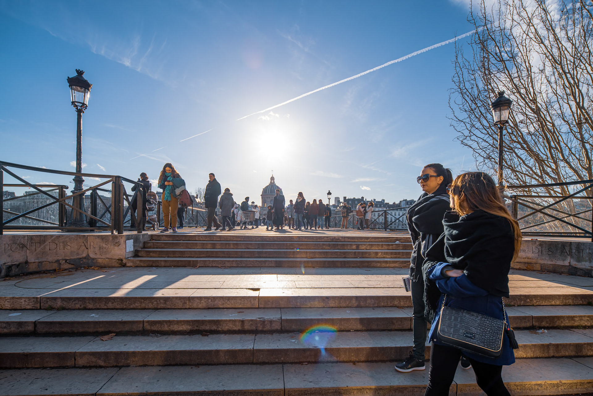 Couples and individuals enjoying the iconic Pont des Arts bridge in Paris under a clear sky.
