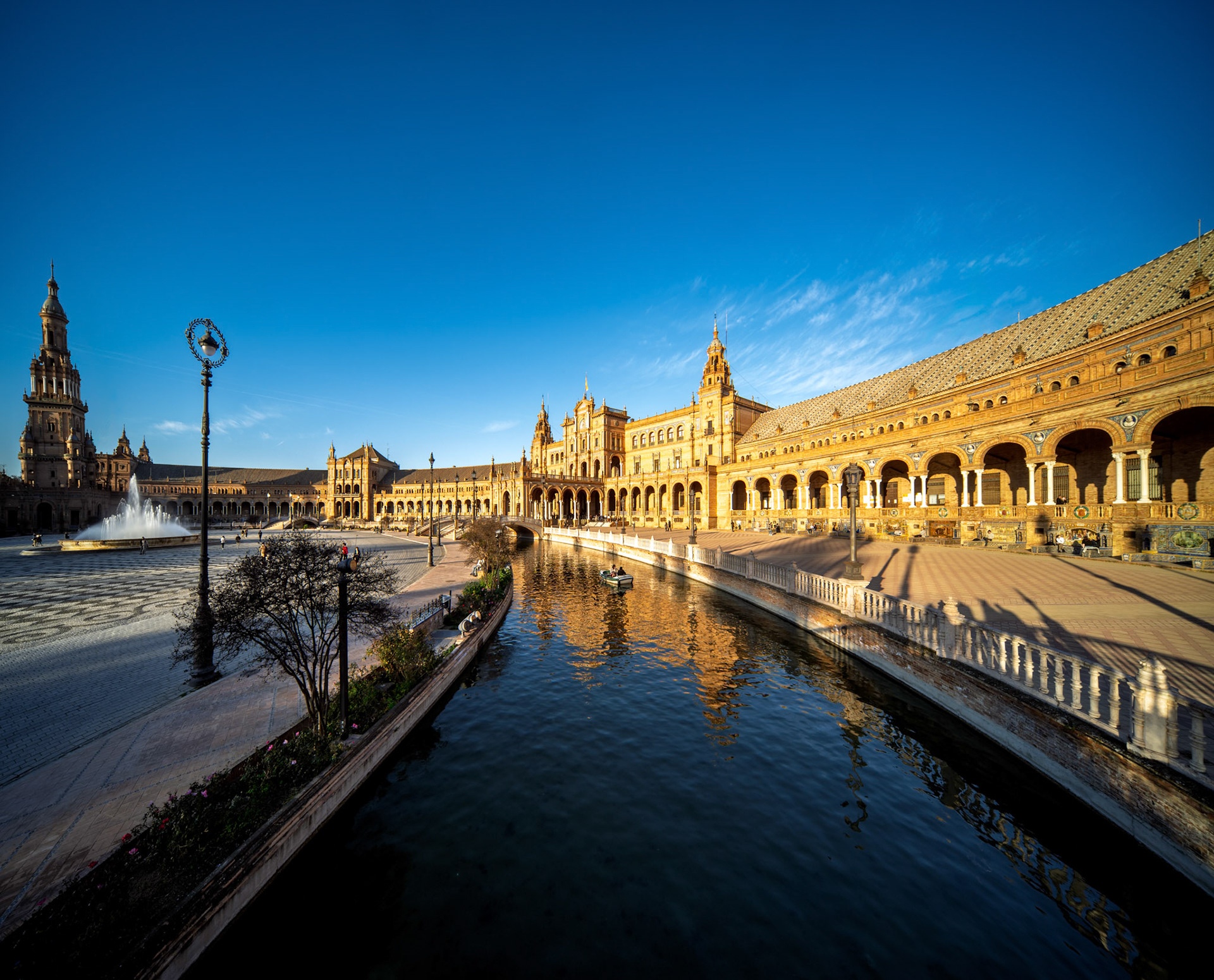 Experience the stunning semicircular design of Plaza de Espana, showcasing its towers, bridges, and canal under a clear sky in Seville.