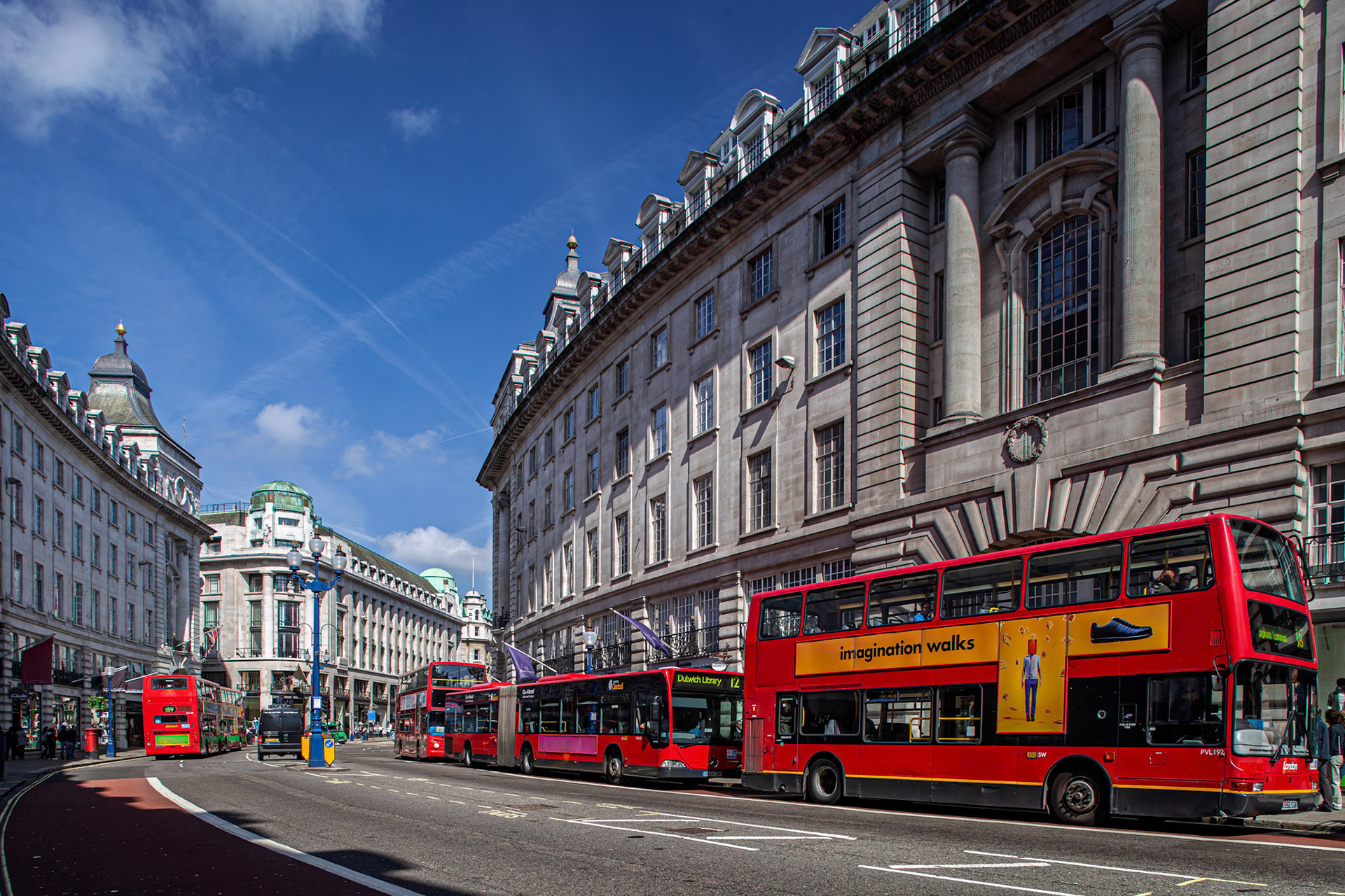 Red double-decker buses line the curved Regent Street in London under a clear blue sky with many people and buildings in view.