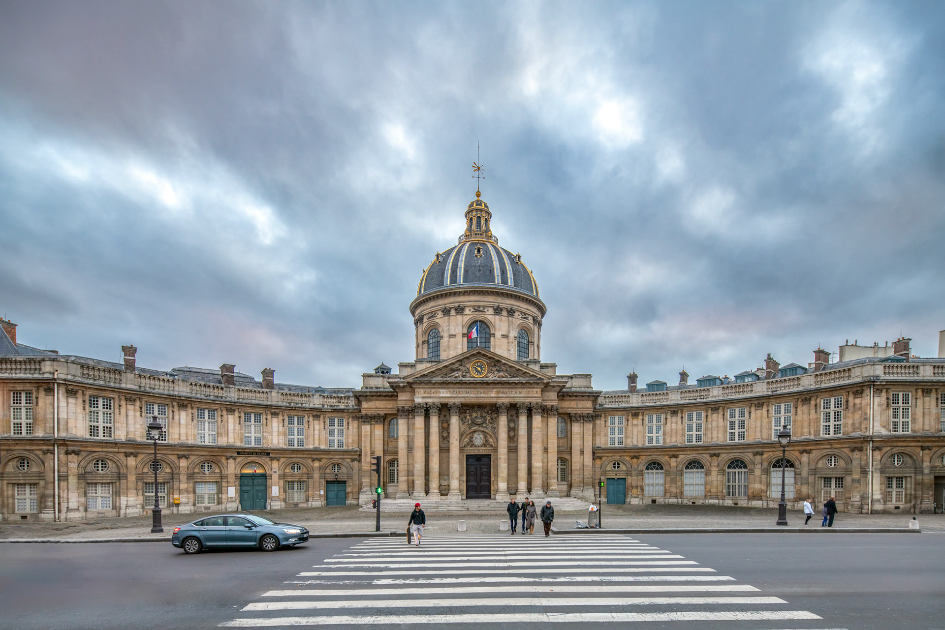 Twilight view of the Institut de France with pedestrians and traffic.