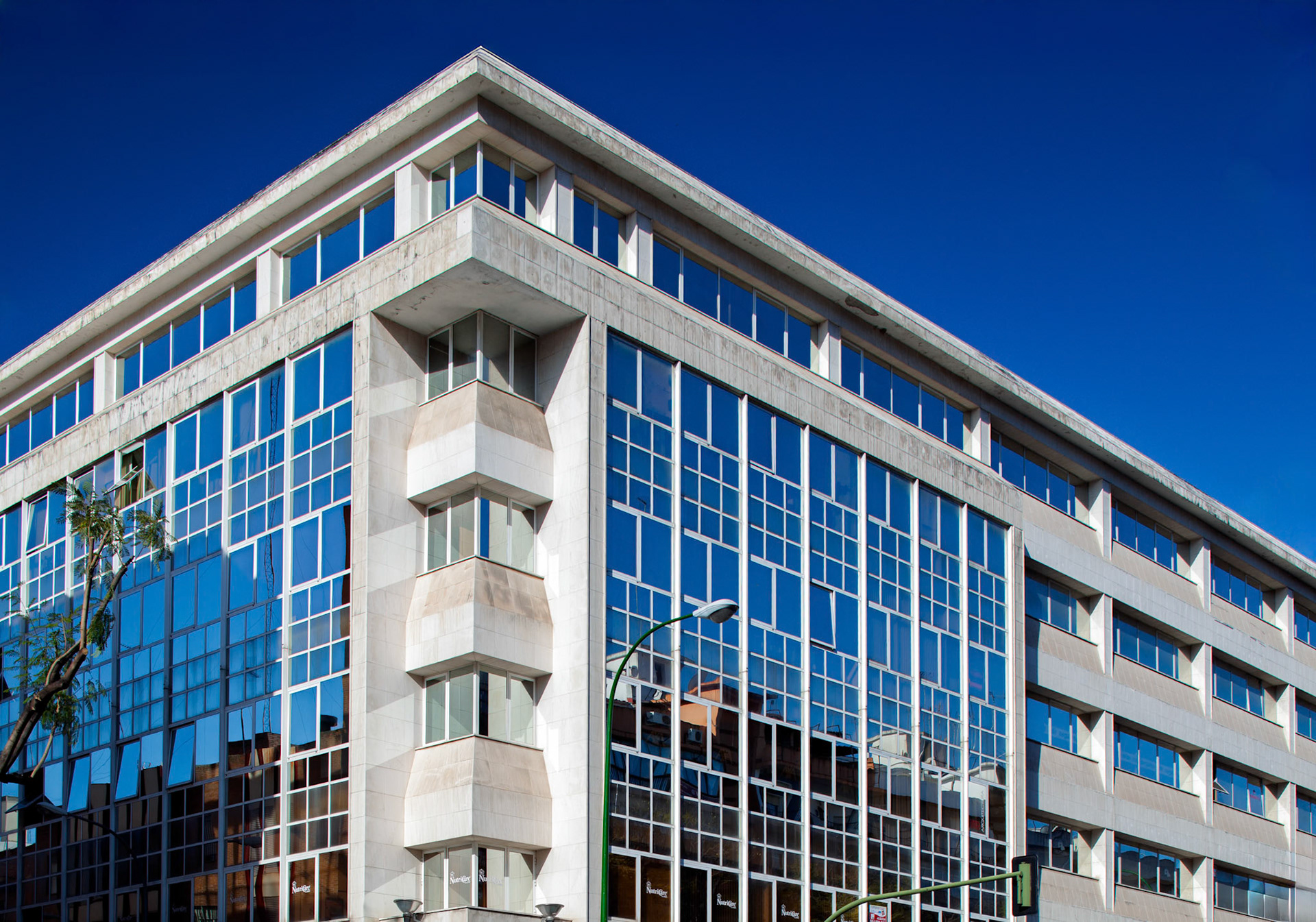 Close-up captures Luis Montoto building in Seville, showcasing its modern glass facade under a vibrant blue sky. Architecture and travel concept.