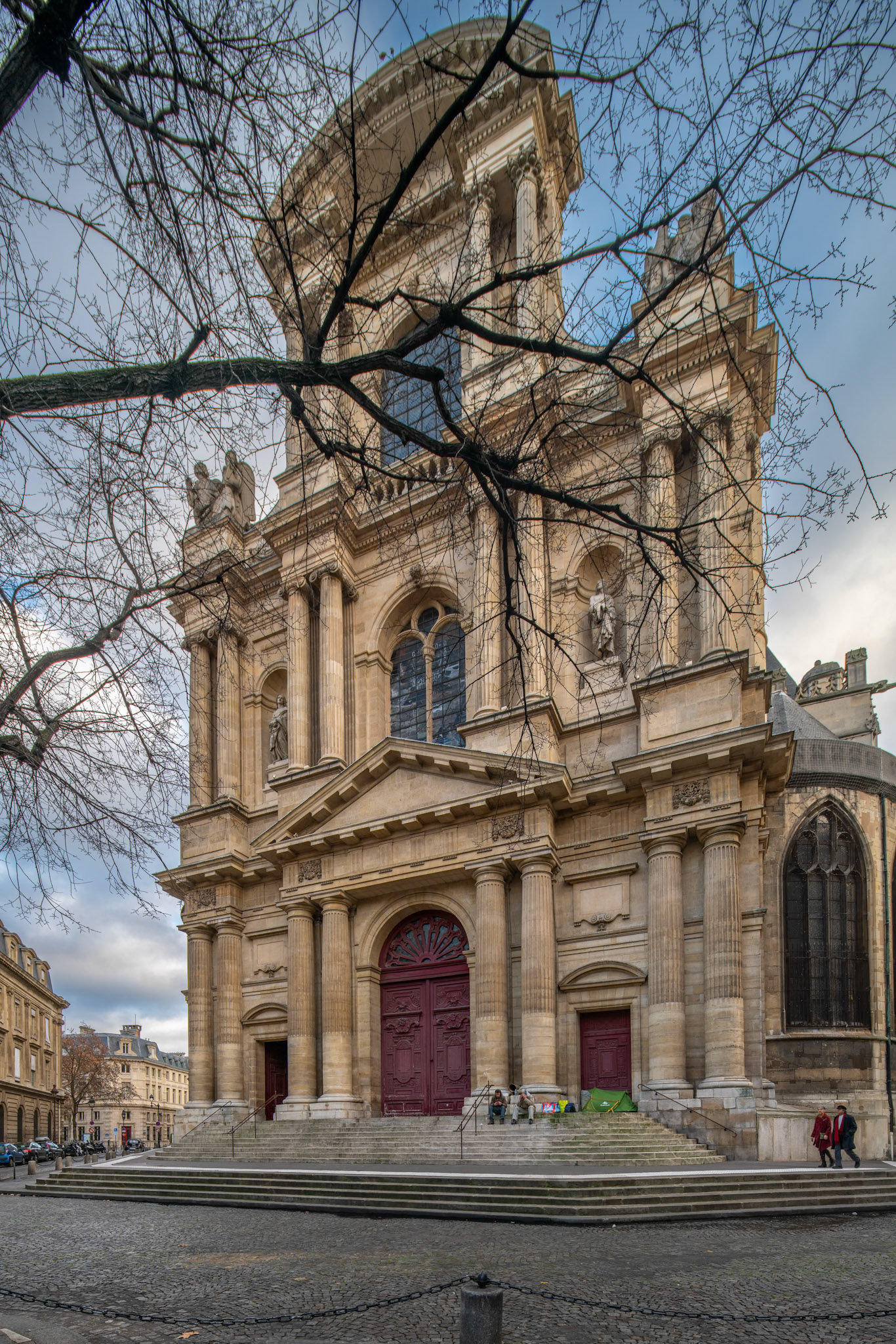The grand facade of Saint-Gervais-Saint-Protais Church in Paris flanked by bare trees.
