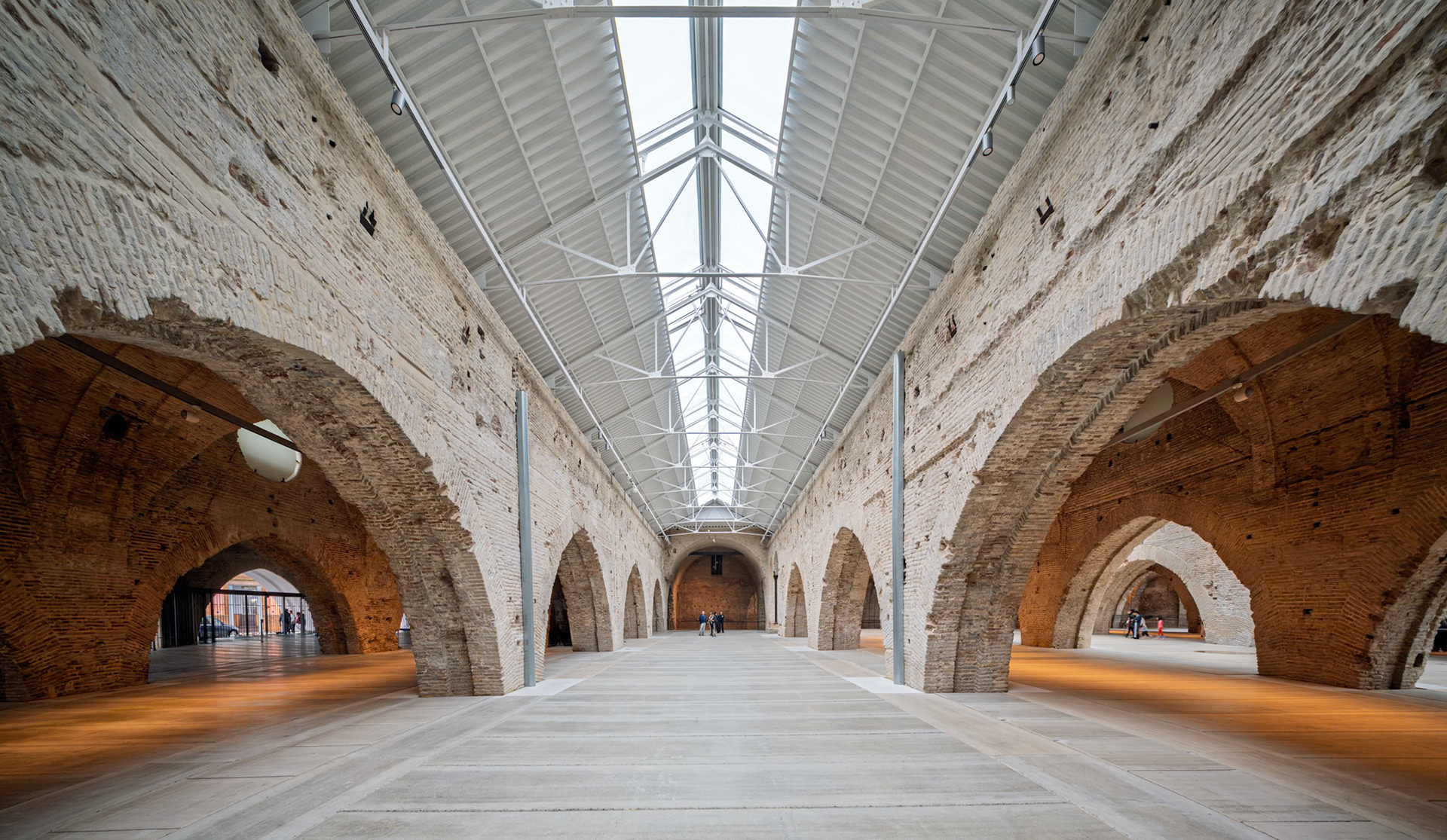 Restored brick arches create a stunning contrast with the modern steel roof in Seville's Atarazanas, showcasing a unique architectural fusion.