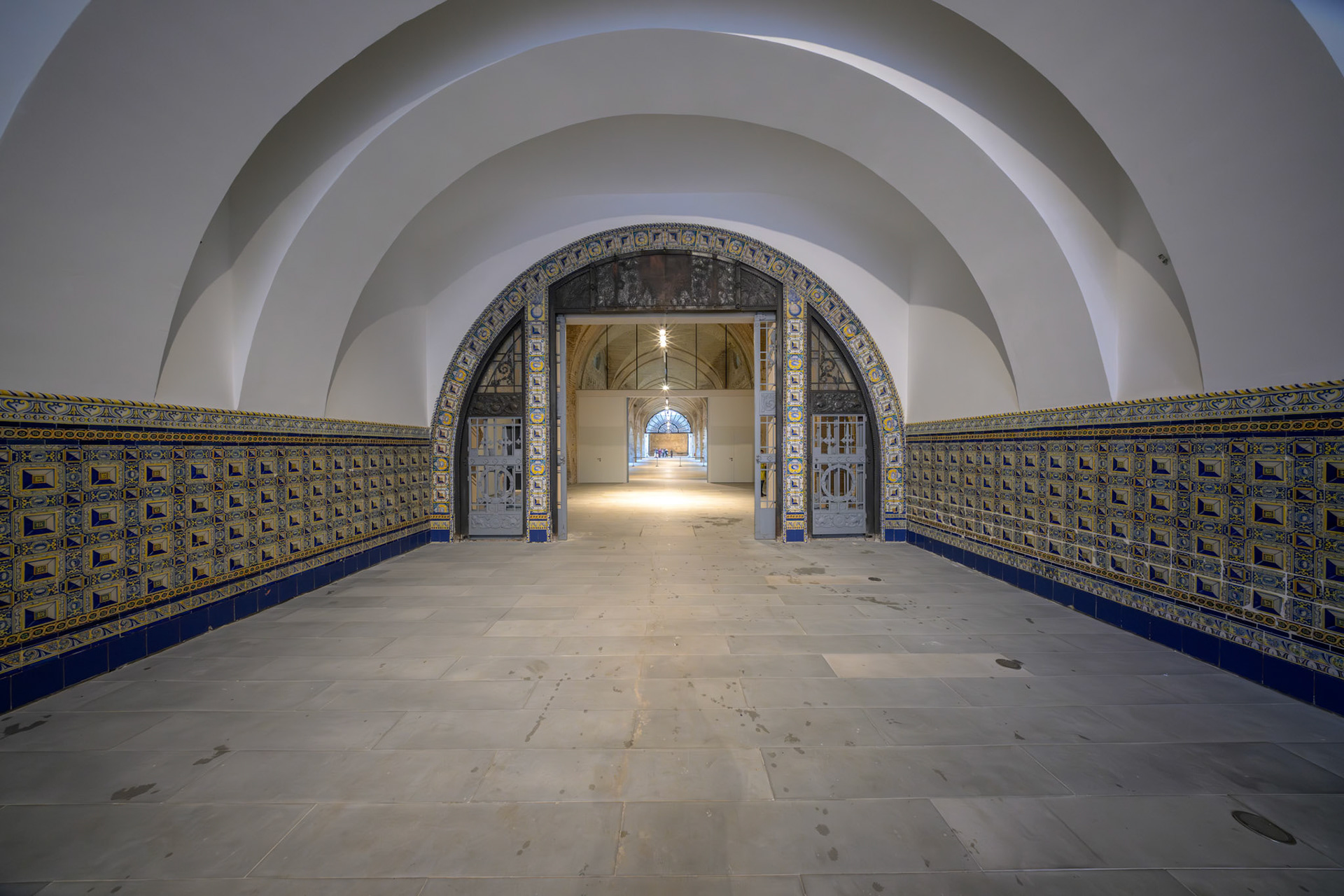 Atarazanas in Seville features a barrel-vaulted entrance hall with intricate tile panels and a grand arch, leading into a spacious central nave.