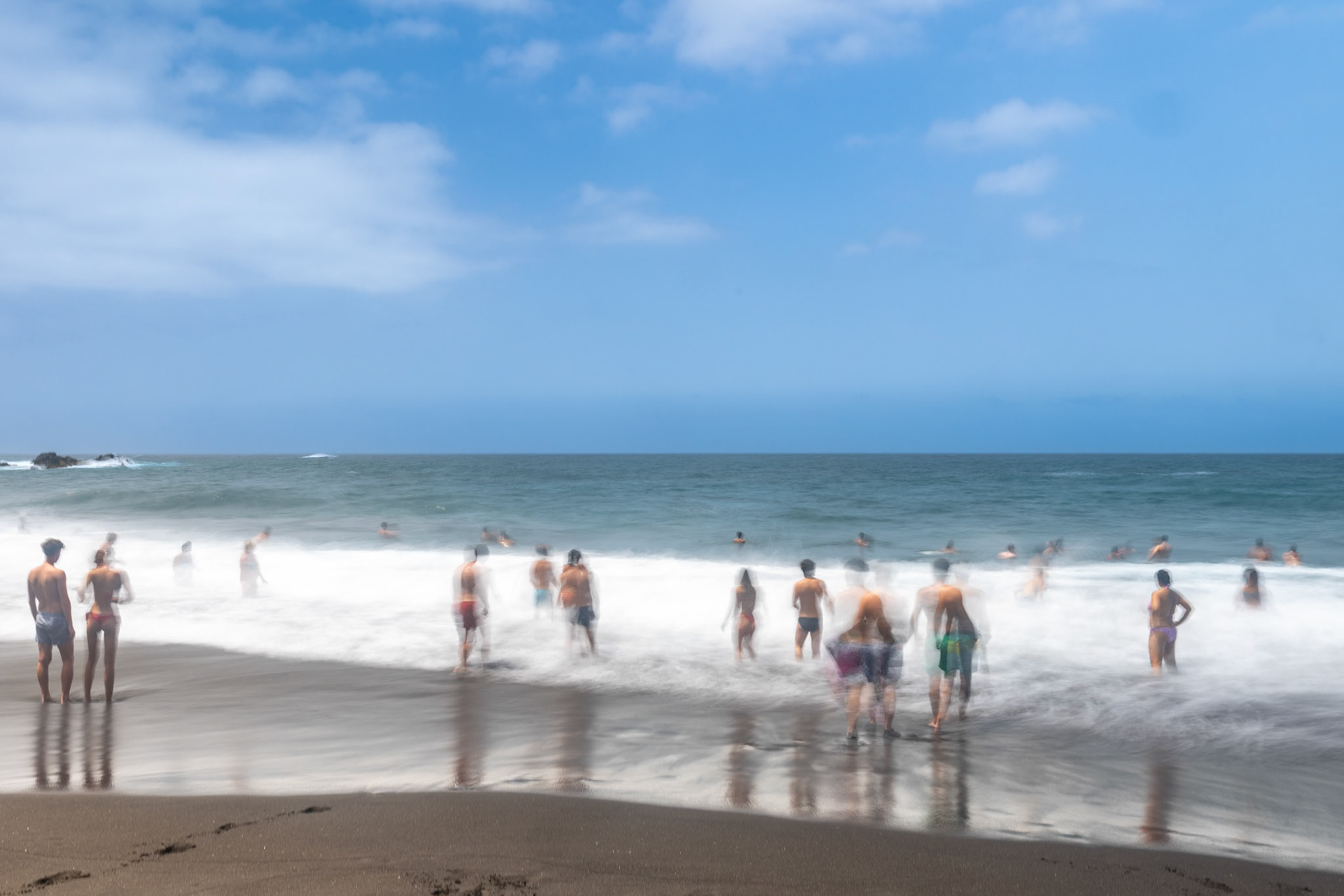 A group of bathers enjoying the waves at Bollullo Beach on the northern coast of Tenerife, La Orotava, Canary Islands, Spain. Long exposure.