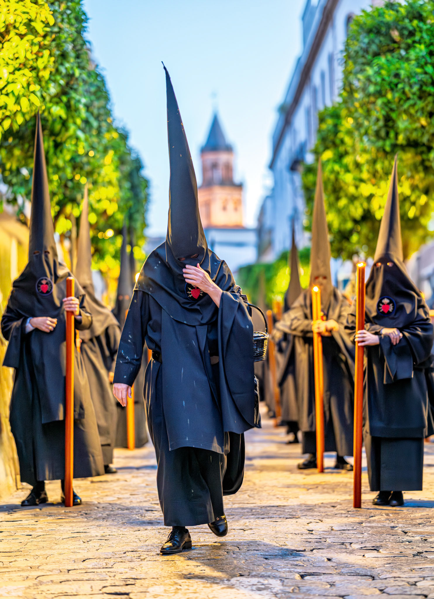A Servitas Brotherhood section marshal carries a collection basket, his habit marked with wax from Nazarenos during a Holy Week procession in Seville, Andalusia, Spain.