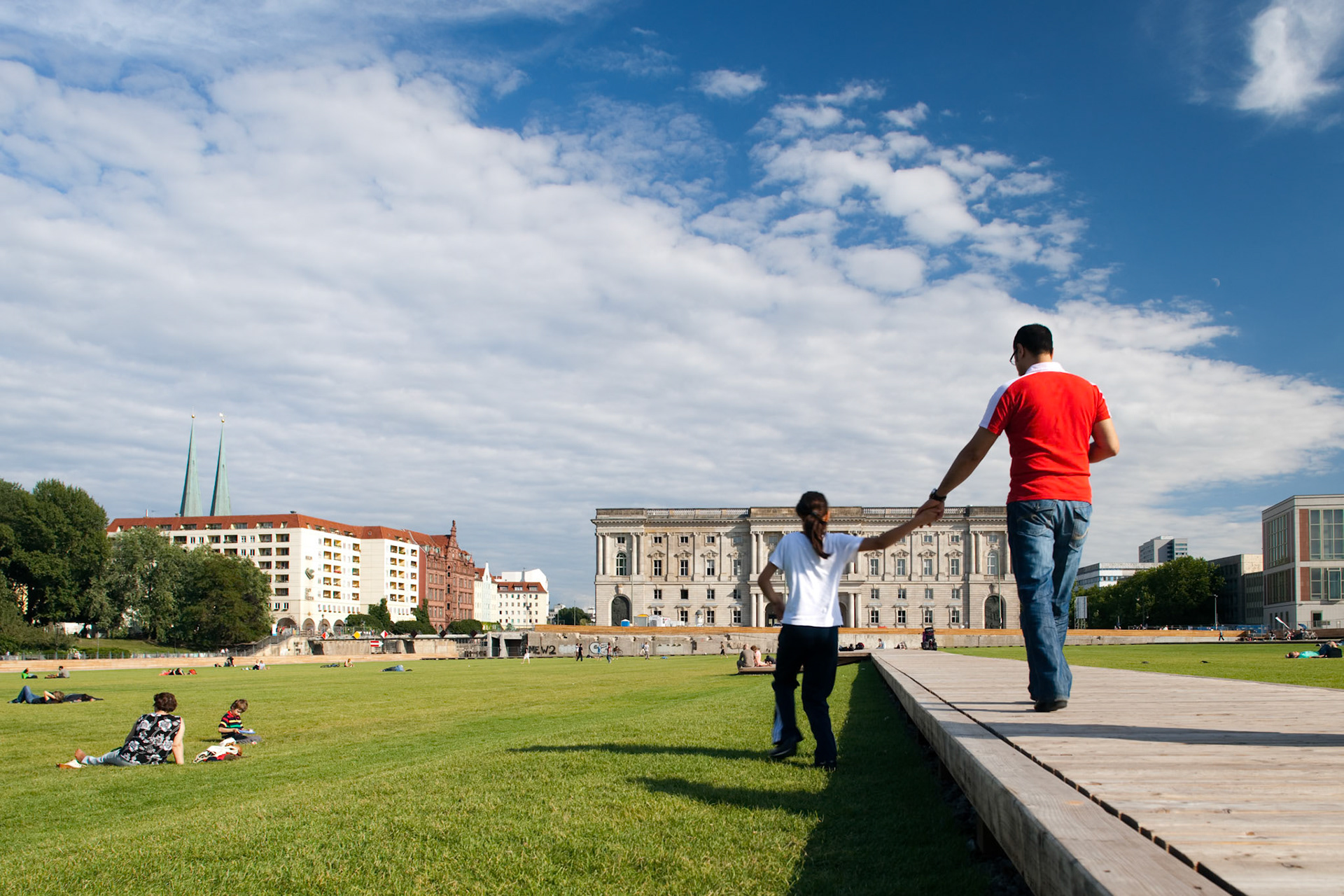 People stroll hand in hand on the lawn at Schlossplatz, enjoying the architecture and warm weather in Berlin\'s bustling Mitte neighborhood.