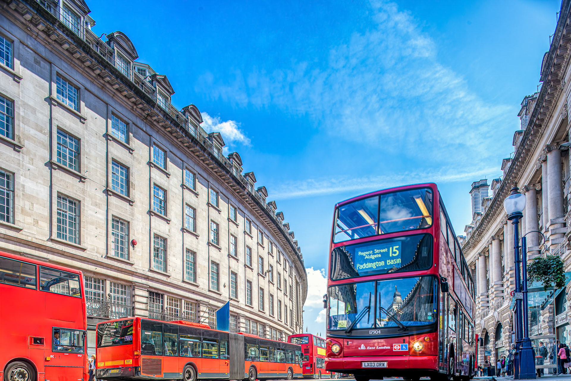 Double-decker buses travel down the bustling Regent Street under a clear blue sky.