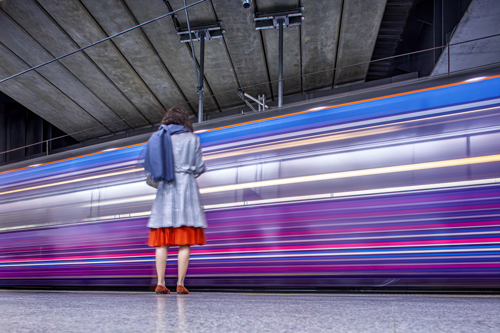 A train arrives at Saint Pancras International Station in London. A woman waits on the platform. The train moves fast, creating a blur of colors.