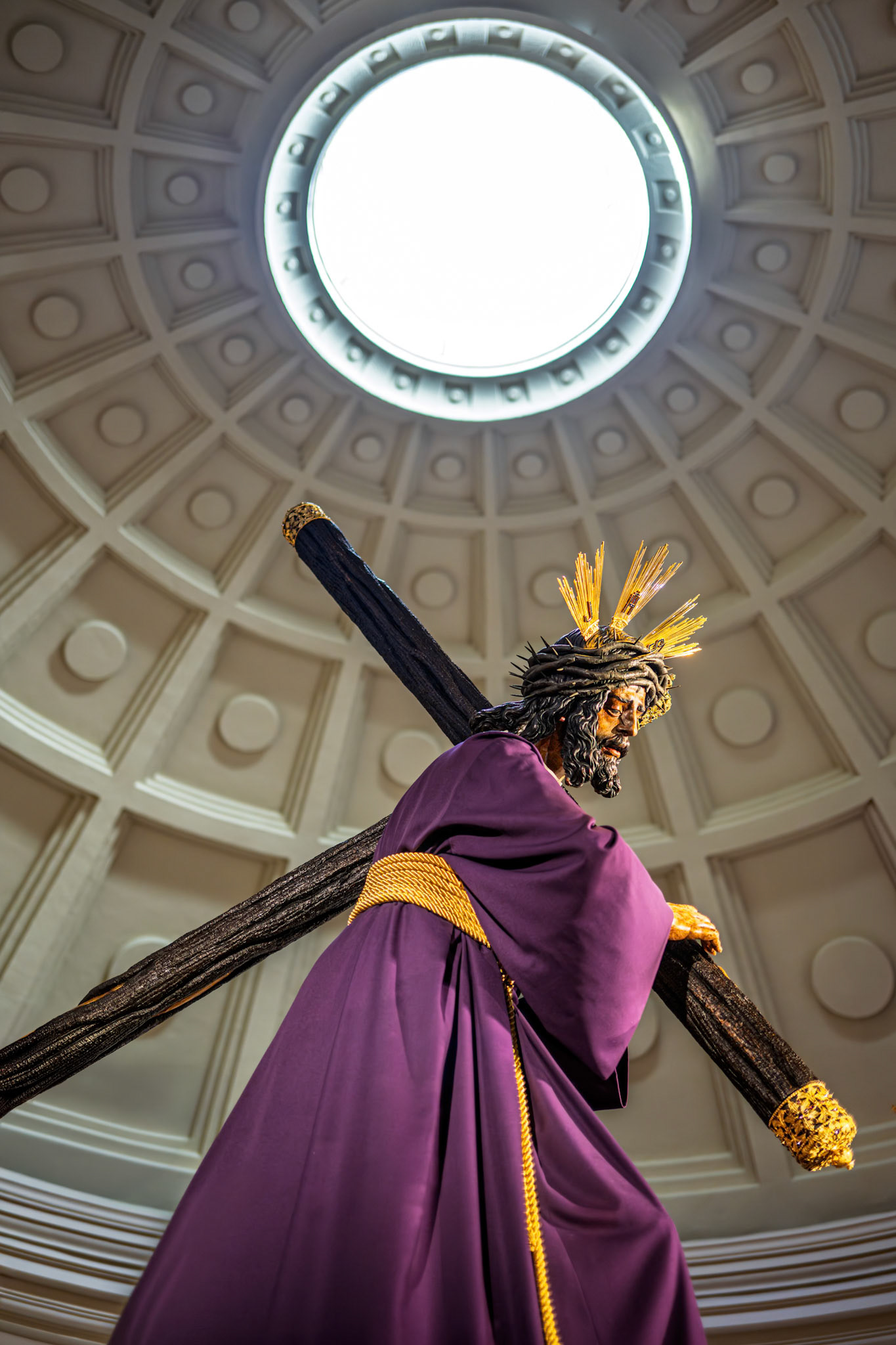 Lord of Gran Poder statue, carrying the cross, stands beneath the illuminating oculus of his basilica's coffered dome during Holy Week in Seville, Spain.