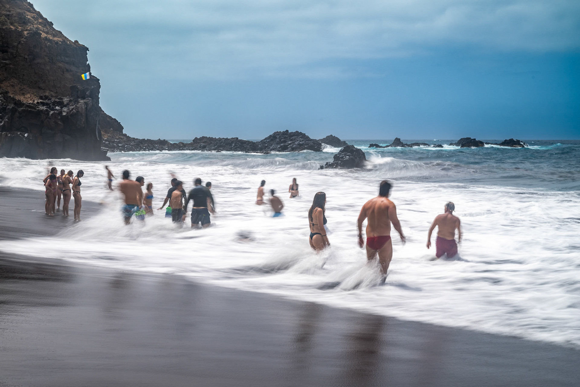Bathers enjoying the waves at Bollullo Beach on the north coast of Tenerife in La Orotava, Canary Islands, Spain. Long exposure shot.
