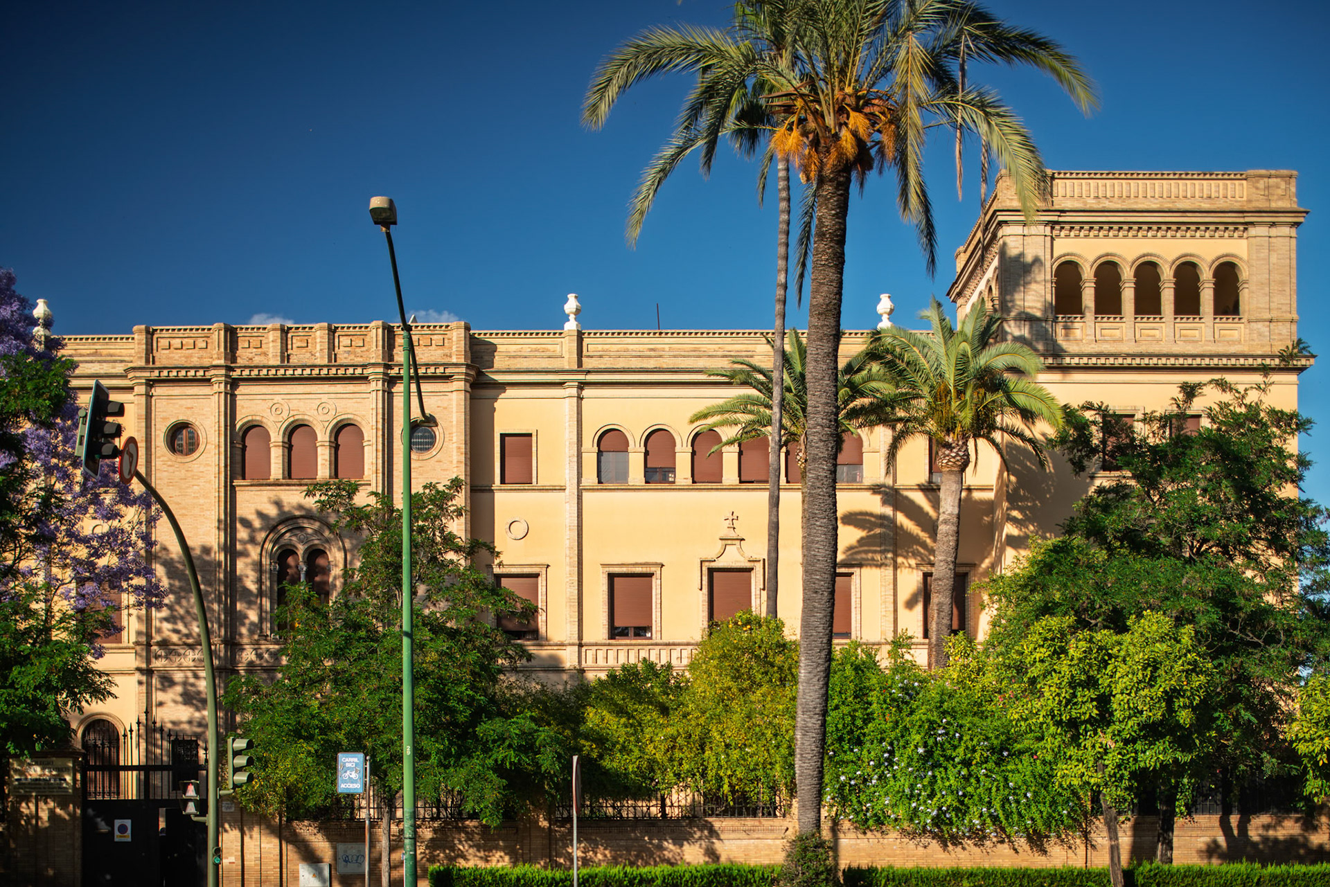 Vicente Traver's 1922 Regionalist building in Seville, now a school, is set amidst lush greenery and palm trees.