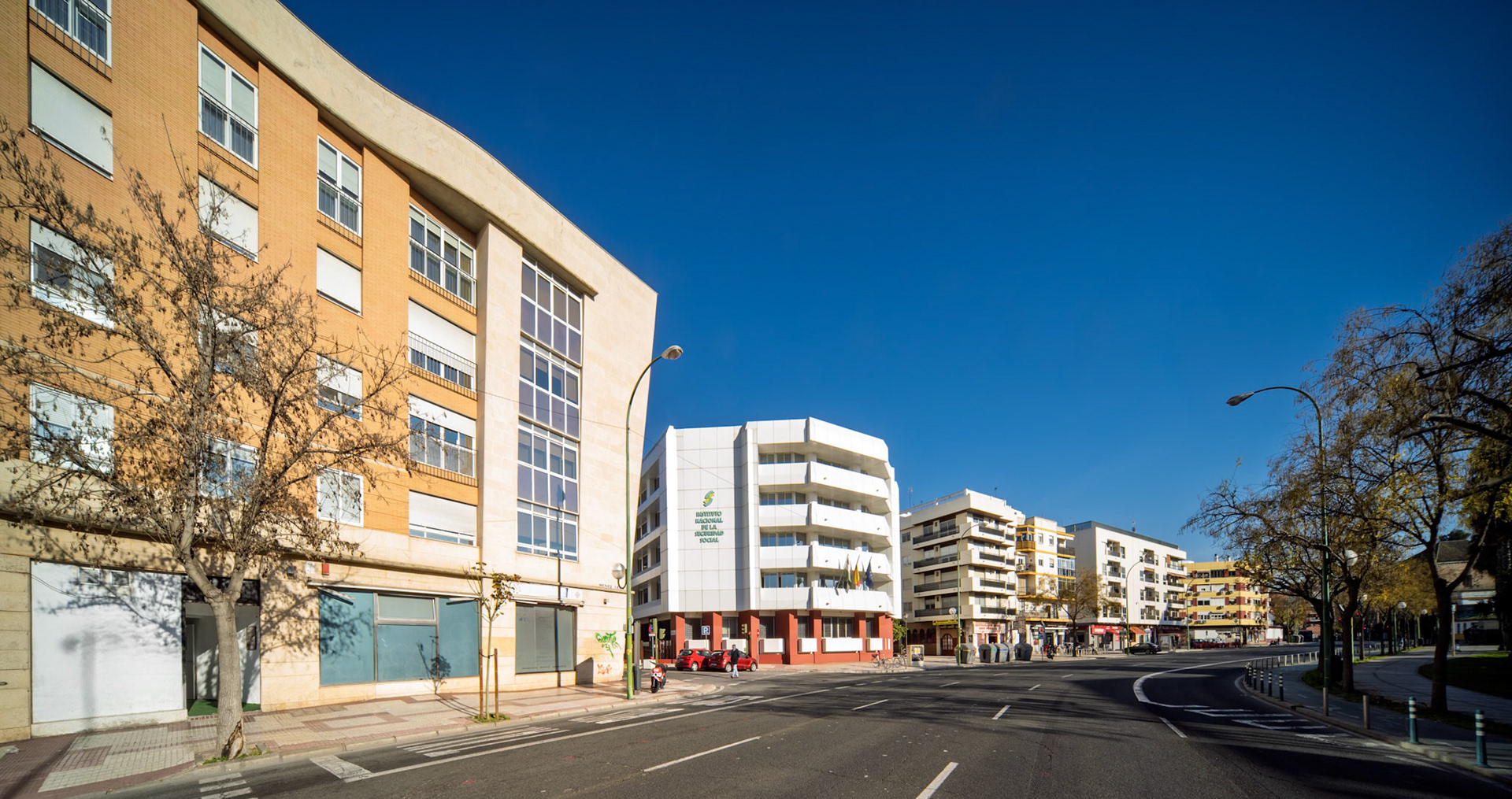 Clean lines of modern buildings frame the Social Security office amid vibrant autumn trees in Seville on a clear day.