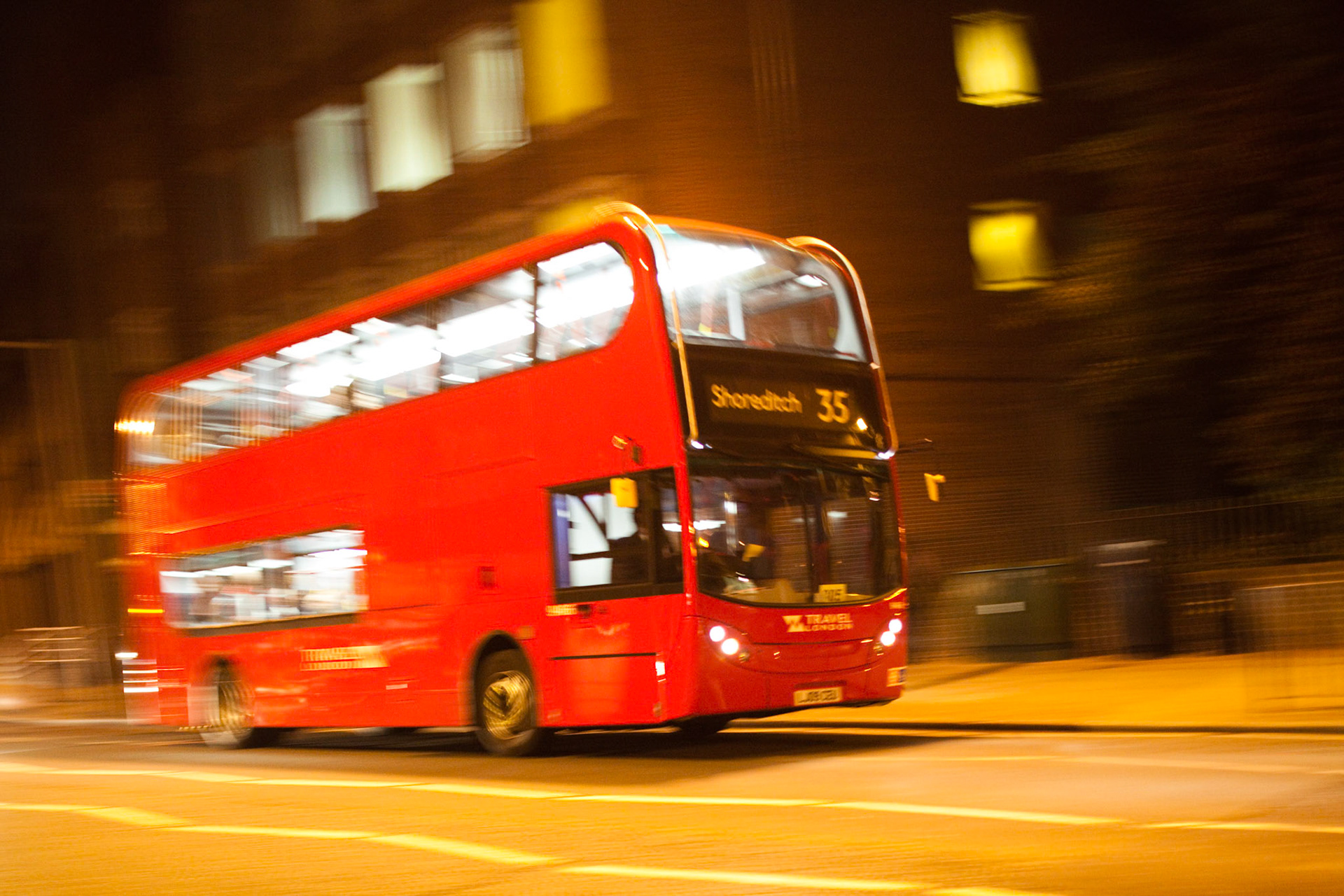 A double decker bus speeds through London streets, illuminated by city lights, showcasing the vibrant atmosphere of the UK capital at night.