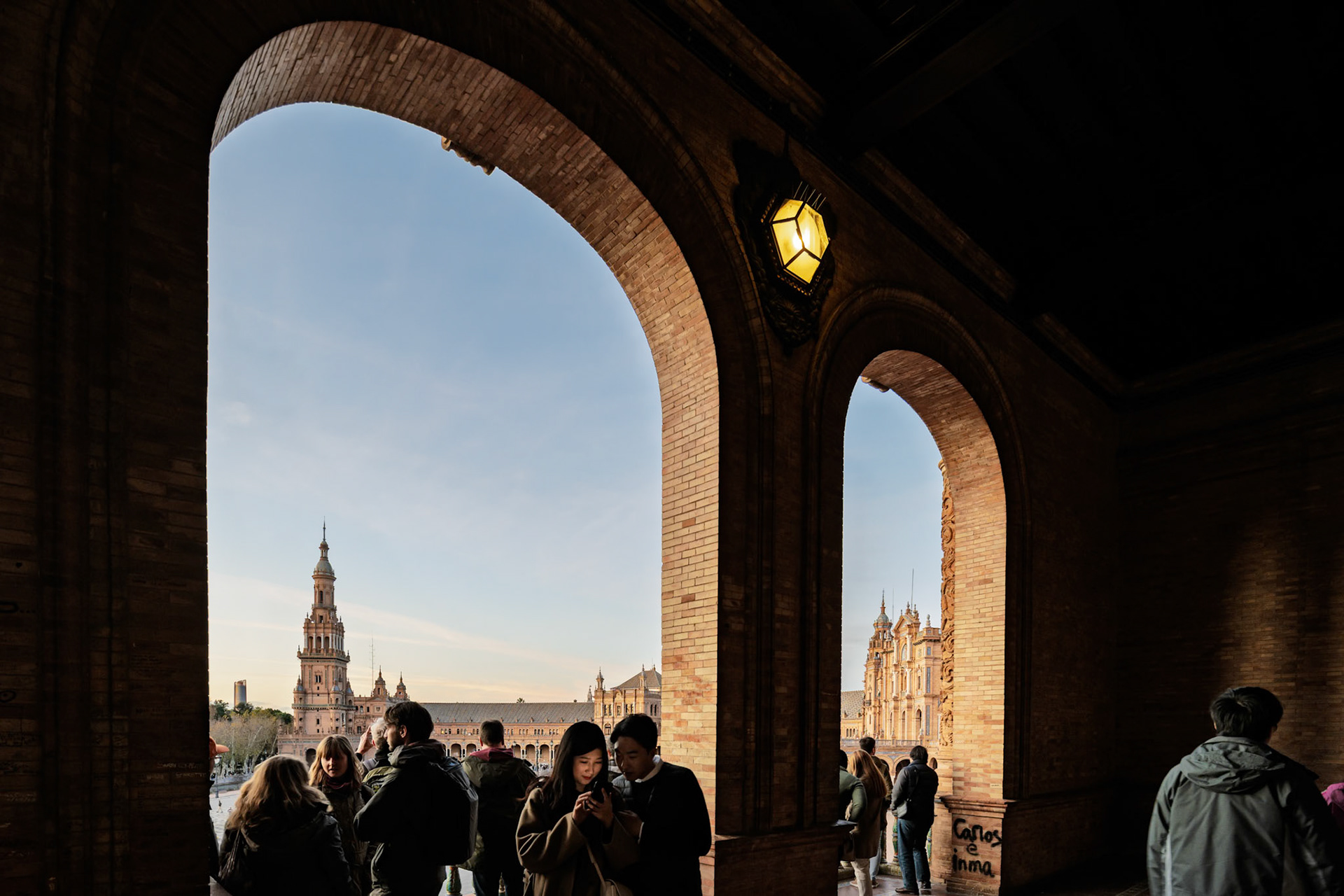 Visitors gather on a balcony, admiring the Renaissance Revival architecture of Plaza de España in the warm late afternoon light.