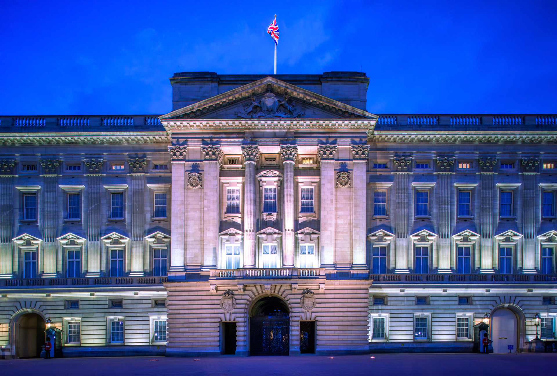Buckingham Palace illuminated at dusk under a soft blue sky.