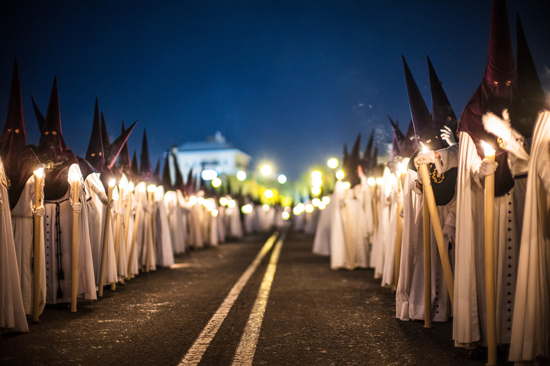 Nazarenes from La Estrella brotherhood in conical hoods and robes carry lit candles during a solemn Holy Week procession on Palm Sunday night in Seville, Andalusia, Spain.