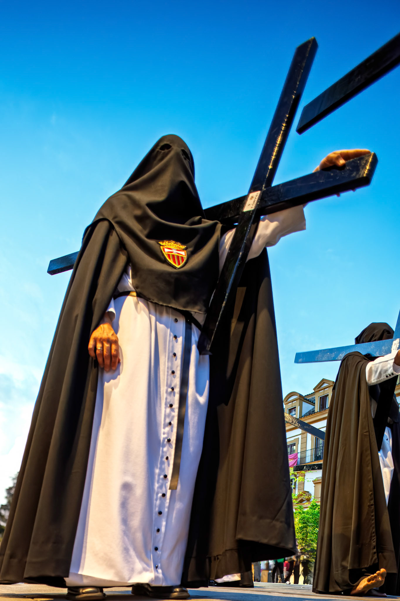 In Seville, penitents from Hermandad de Santa Genoveva carry wooden crosses in solemn reflection during Holy Week observances.