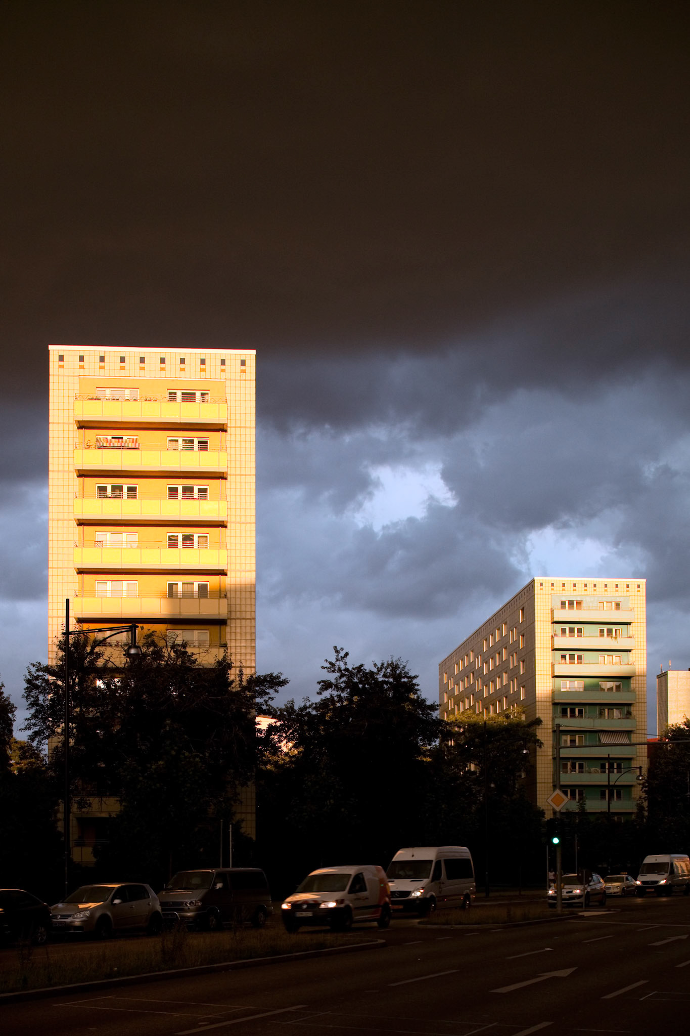Apartment buildings on Alexander Street in East Berlin glow during sunset amid dramatic clouds and natural light contrasts.