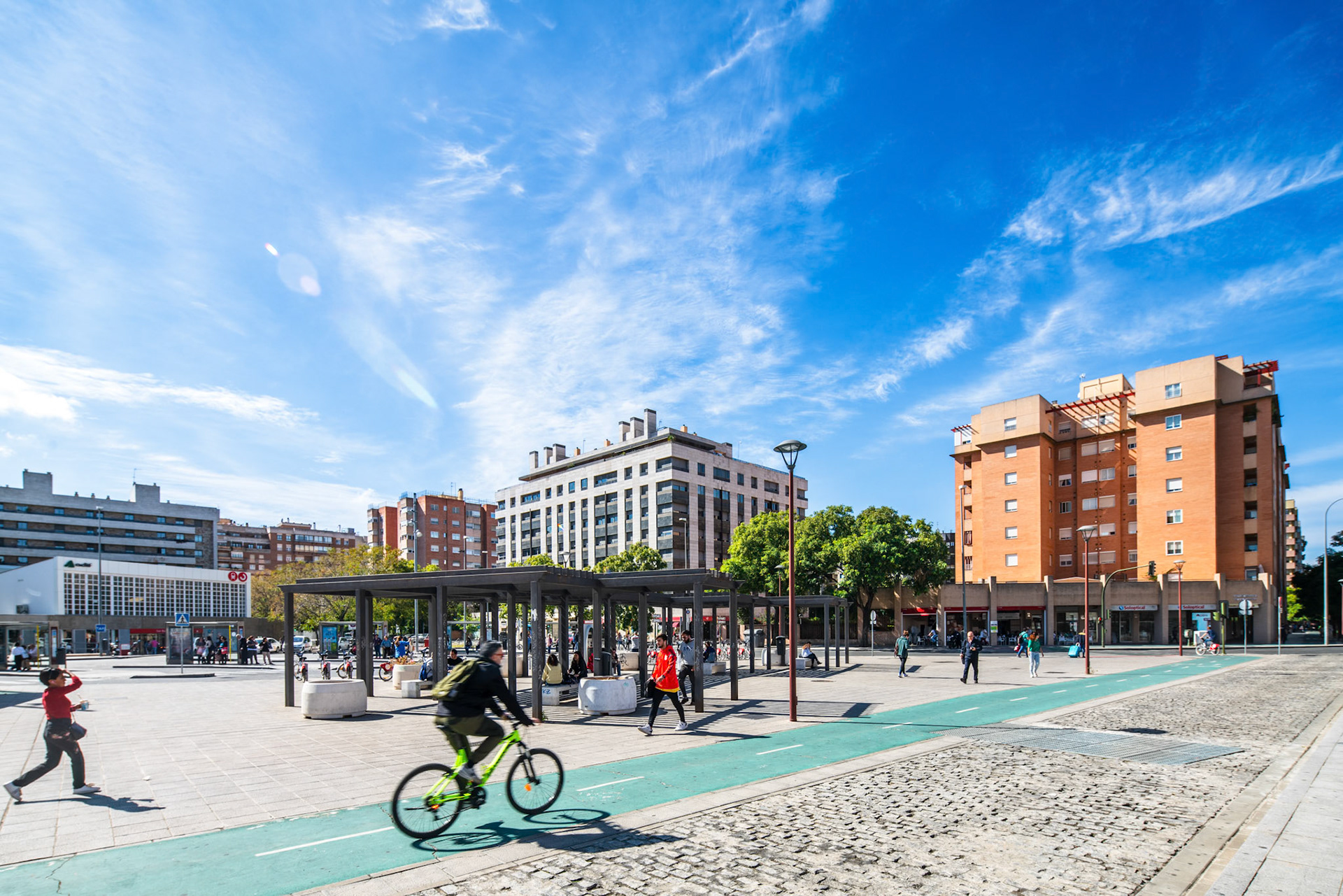 Pedestrians and a cyclist move about the plaza outside San Bernardo station under blue skies.