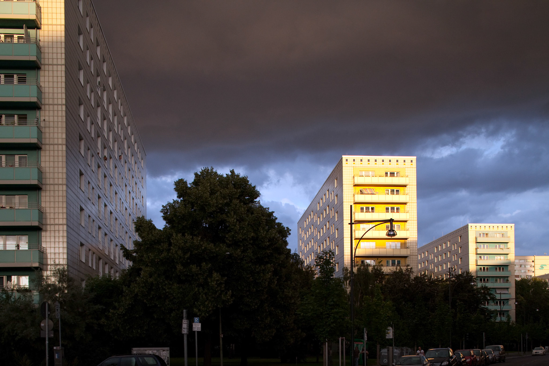 Apartments on Alexander Street in East Berlin are illuminated by evening light amid gathering storm clouds.