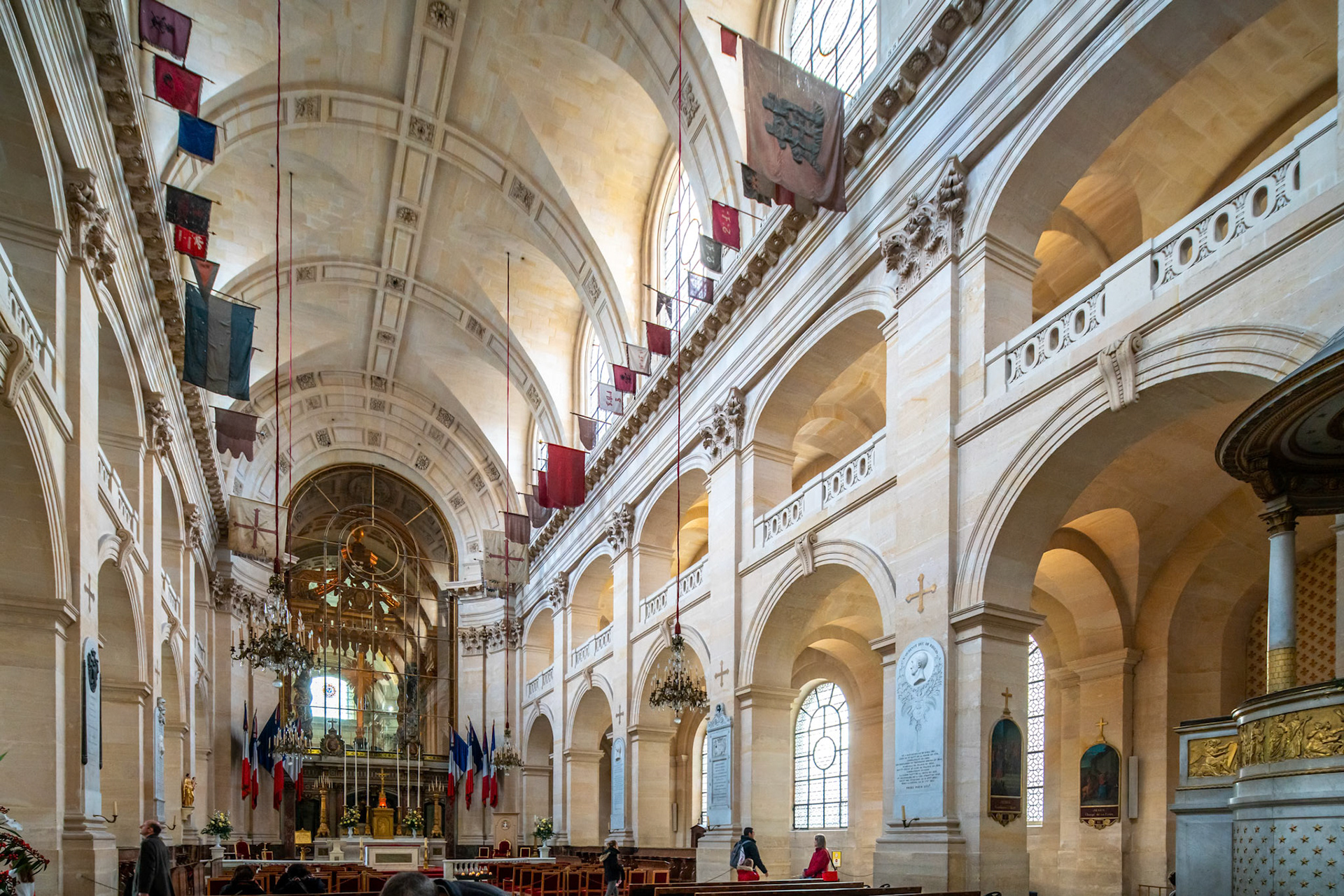 The interior of La Catedral de Saint-Louis-des-Invalides in Paris, France, featuring high vaulted ceilings and flags suspended from the ceiling.