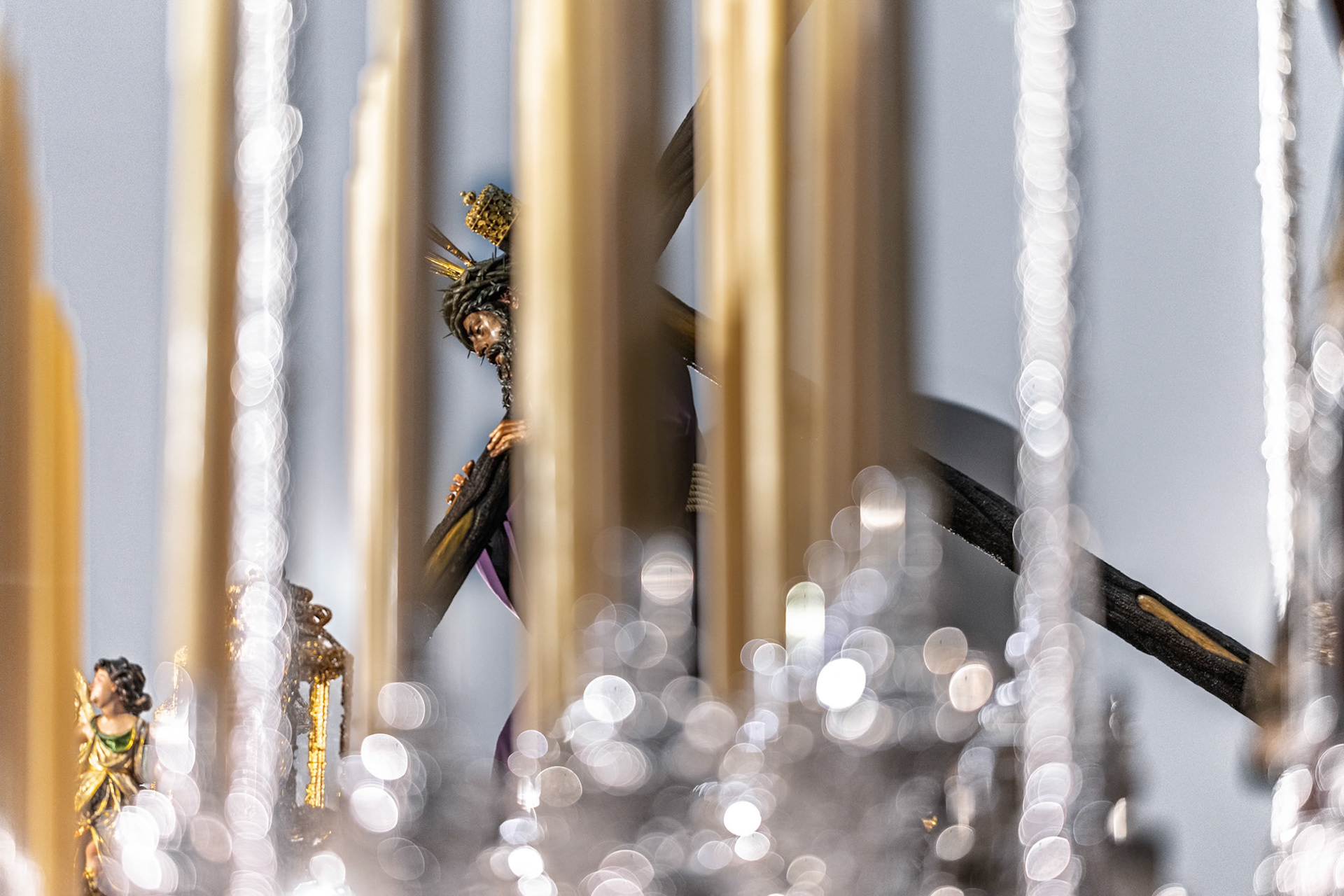 Christ of Gran Poder statue viewed through canopy poles and candles of the Virgin of Mayor Dolor's palio float. Holy Week procession, Seville, Spain.