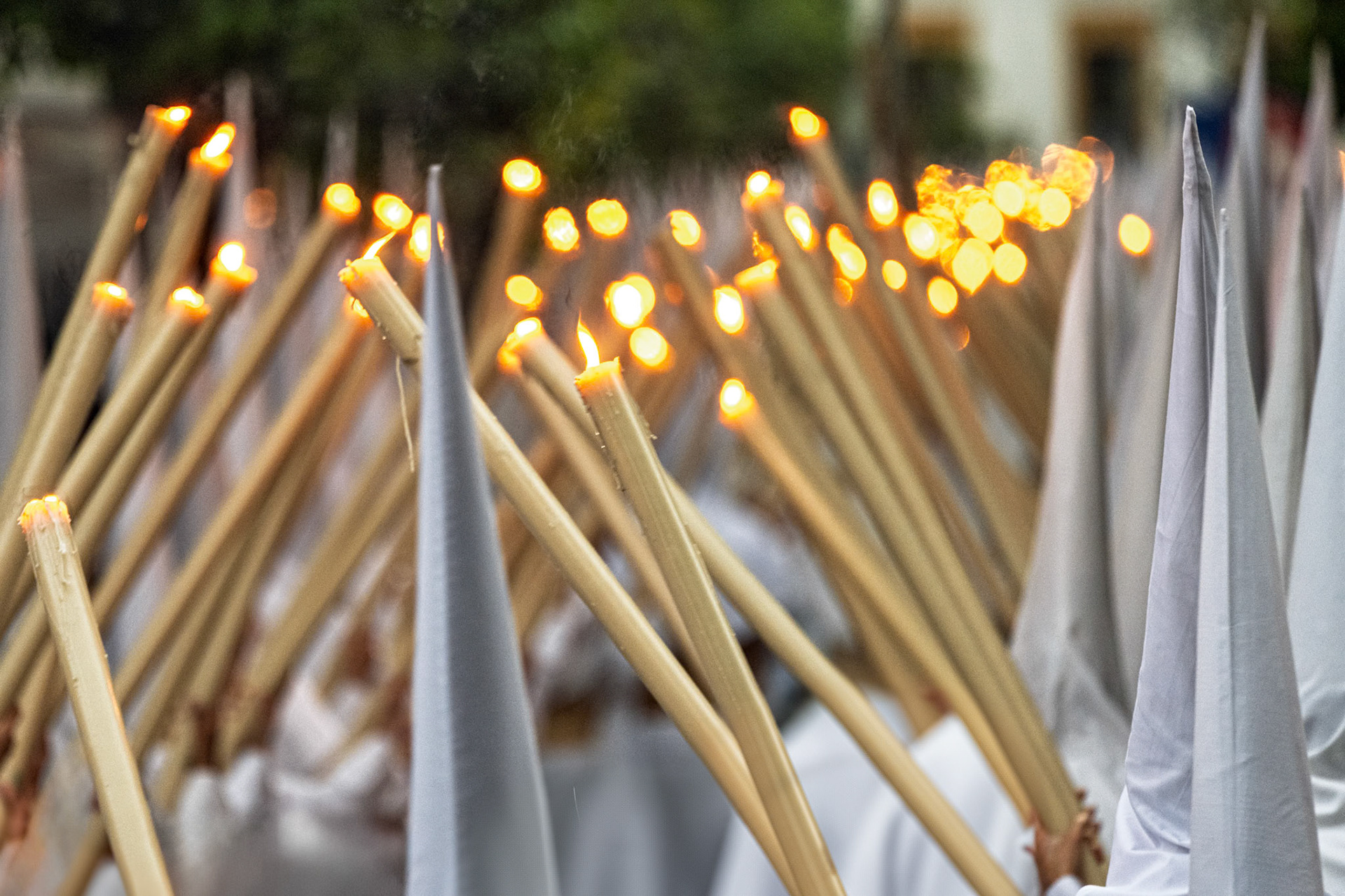 Tight rows of white nazarenos from the Amargura Brotherhood carry lit candles on Palm Sunday during Holy Week in Seville, Andalusia, Spain.