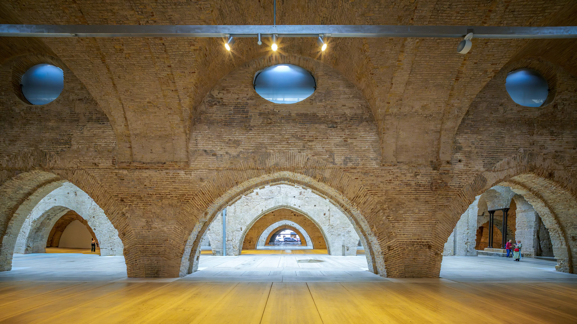 Vaulted brick arches create a rhythmic sequence inside Seville's historic Atarazanas shipyard, showcasing its medieval engineering and architecture.
