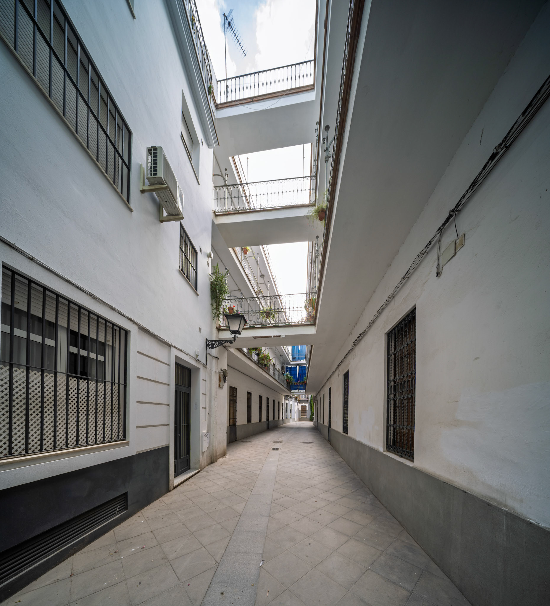 Pasaje Valvanera—social housing corridor designed in 1915 by Manuel Martín, with tiled paving and overhead galleries linking modest dwellings in Seville’s historic core.
