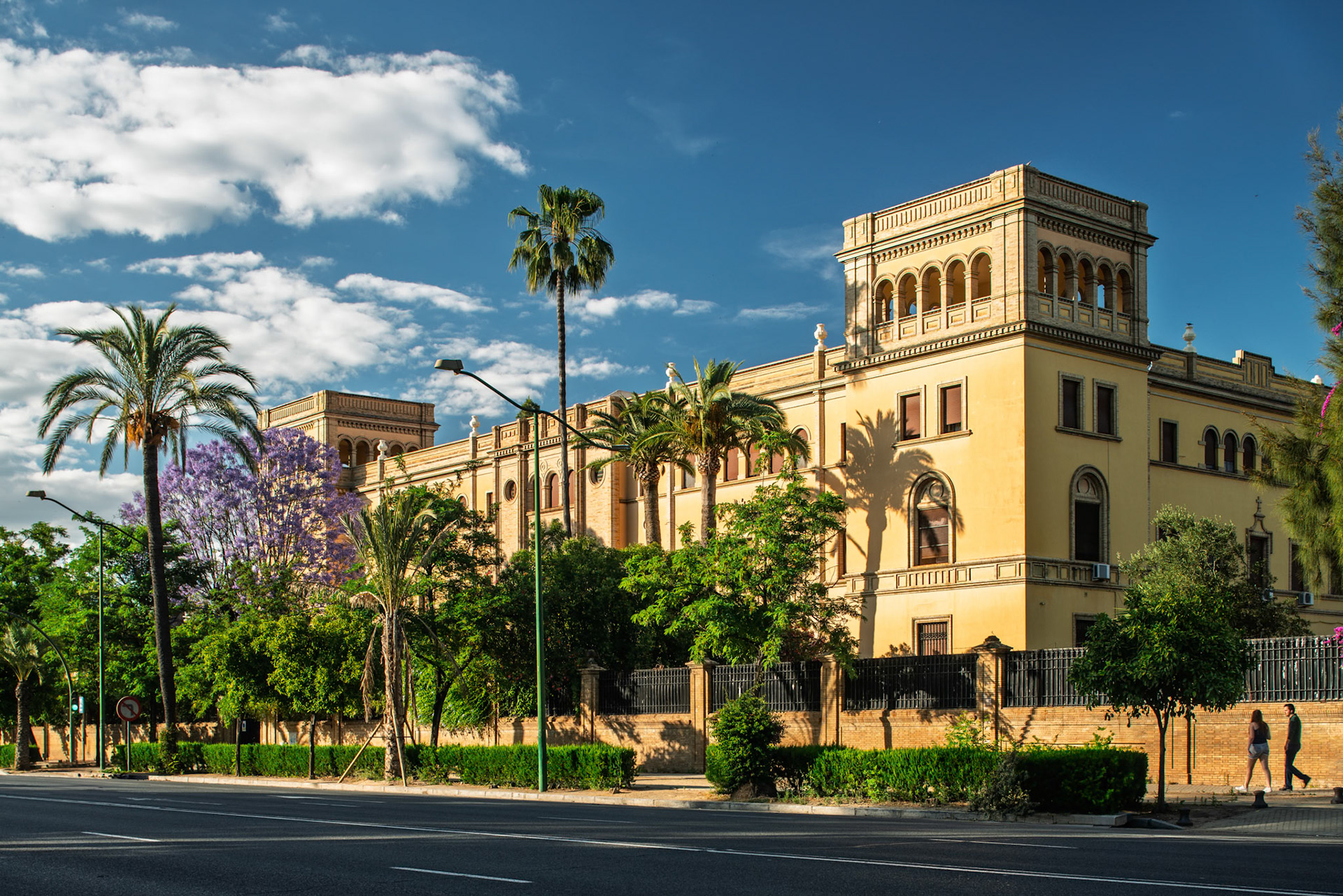 Beautiful regionalist-style building in Seville features palm trees and colorful foliage, housing a school since its construction in 1922.