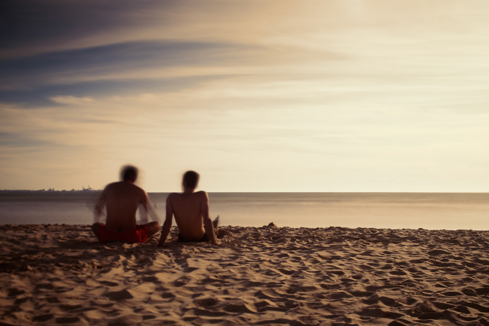 Two boys sitting on the beach and staring at the sea. Daylight long exposure shot by the use of neutral density filters.
