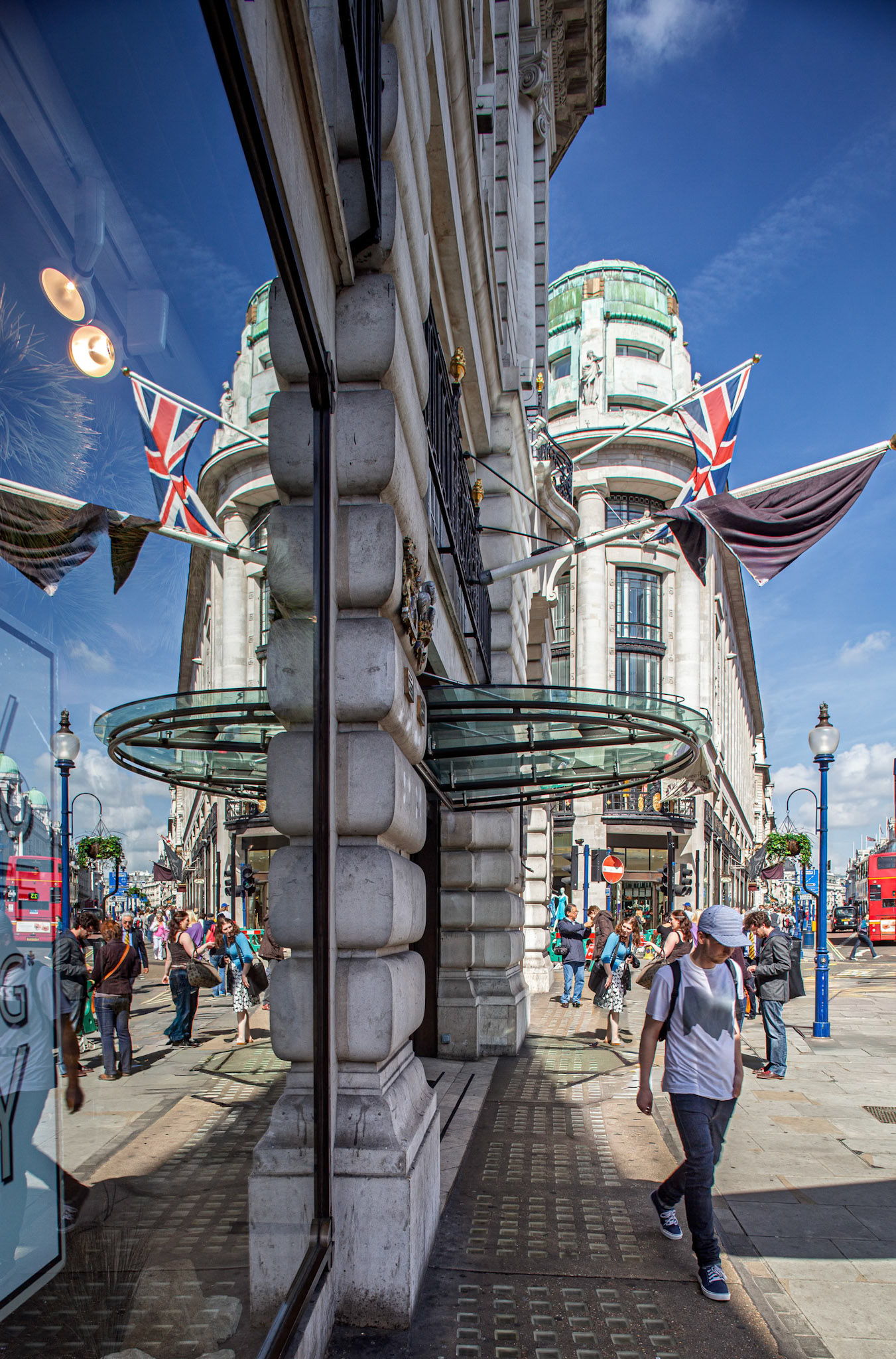 People walk along Regent Street in London, while flags hang above and shop reflections show the vibrant life of the city.